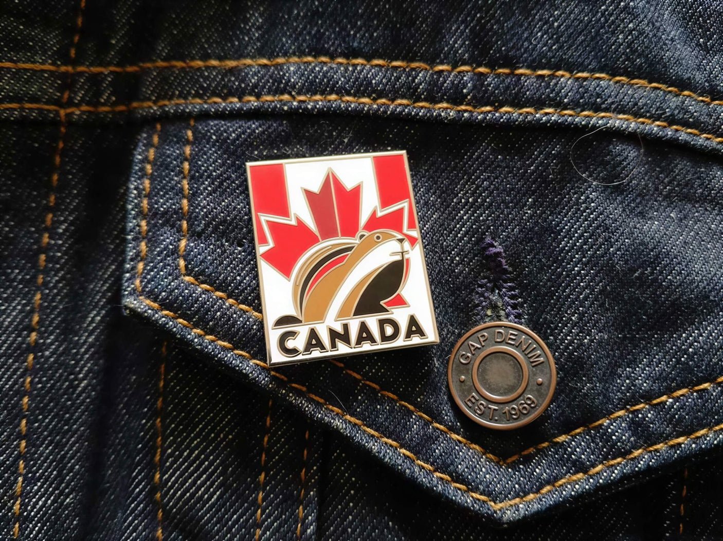 Canada enamel pin featuring a beaver and maple leaf design, attached to a denim jacket pocket.