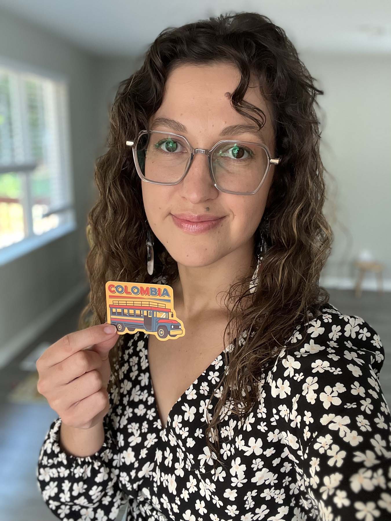 Colombia sticker with a colorful bus design, held by a person with curly hair in a black floral blouse.