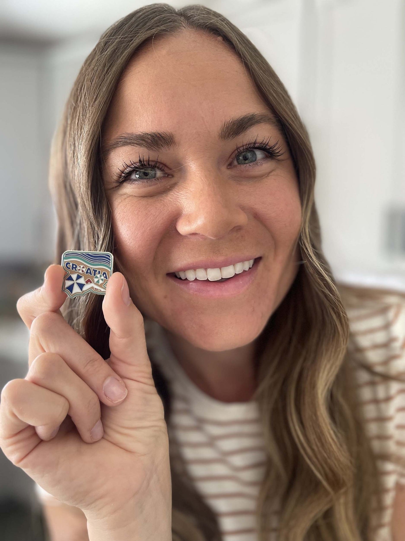 Croatia enamel pin held by a woman, featuring blue and white geometric shapes with the word "Croatia" at the top.