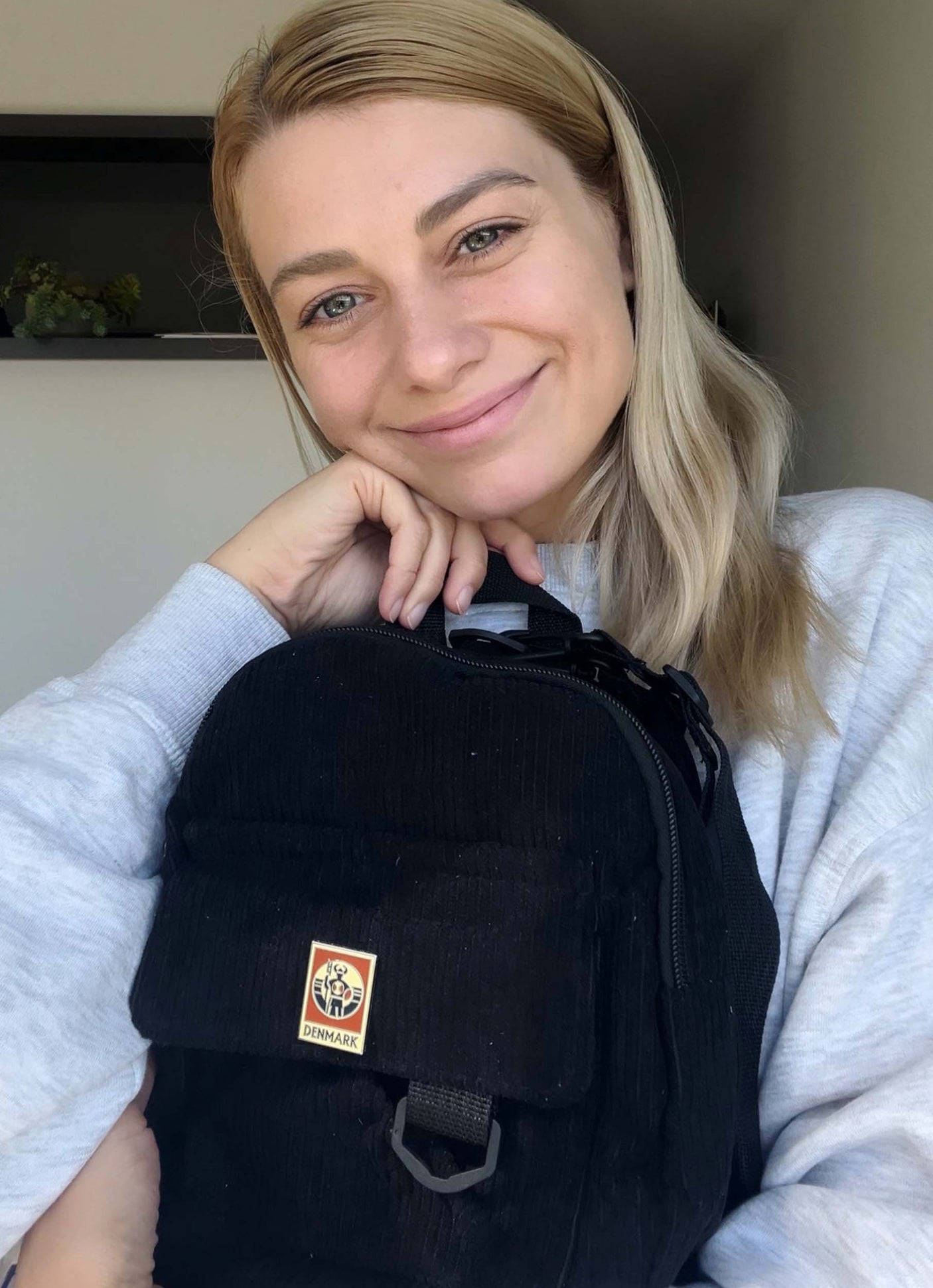 Denmark enamel pin attached to a black backpack, held by a smiling woman with long blonde hair.