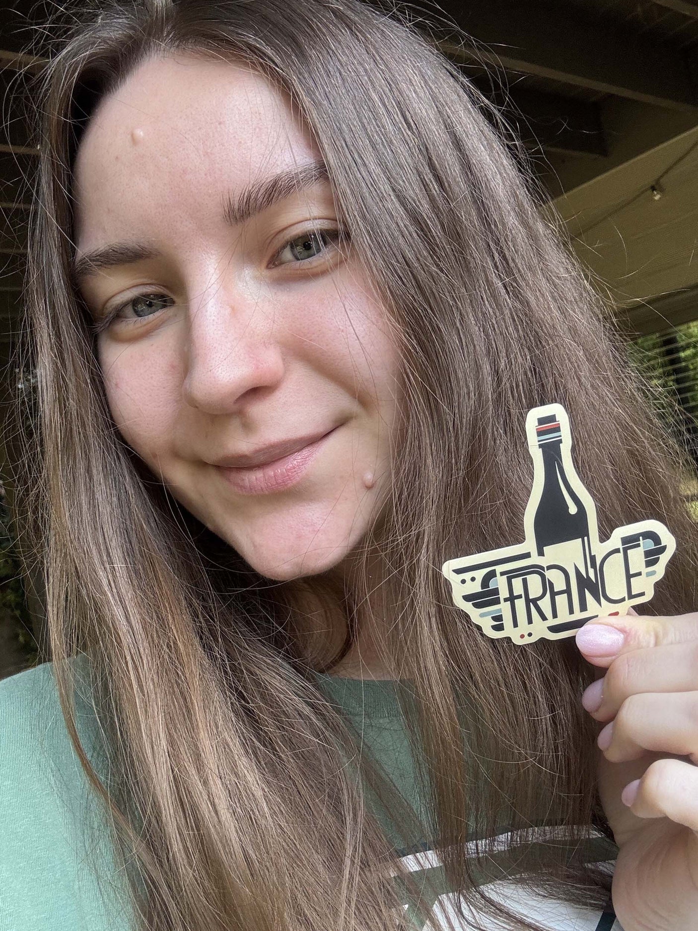 A woman with long hair holds a France sticker featuring a wine bottle design.