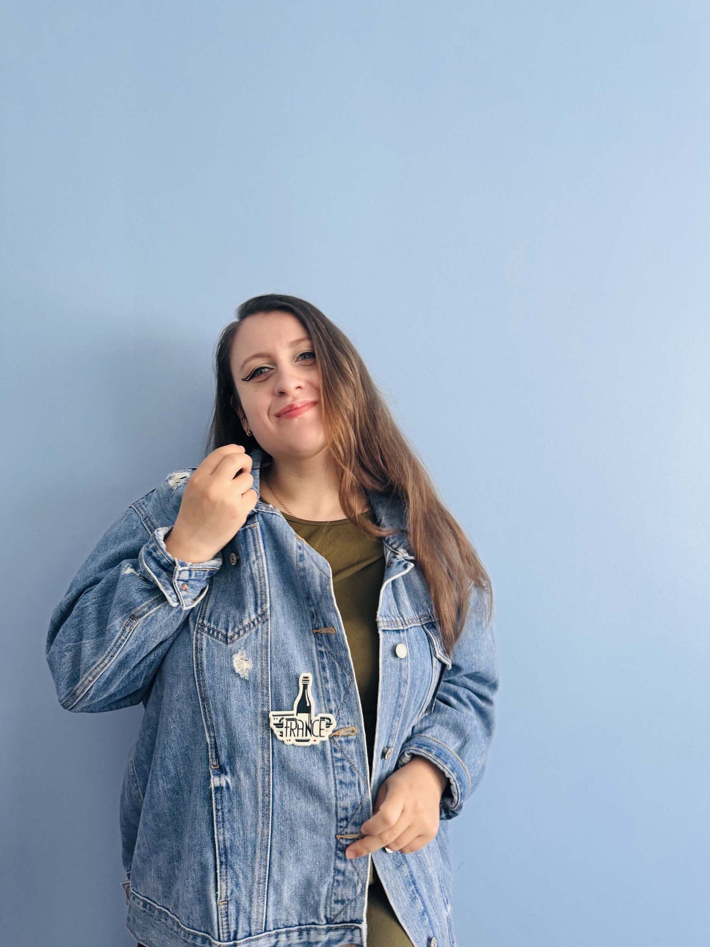 France patch on a denim jacket worn by a woman against a light blue wall.