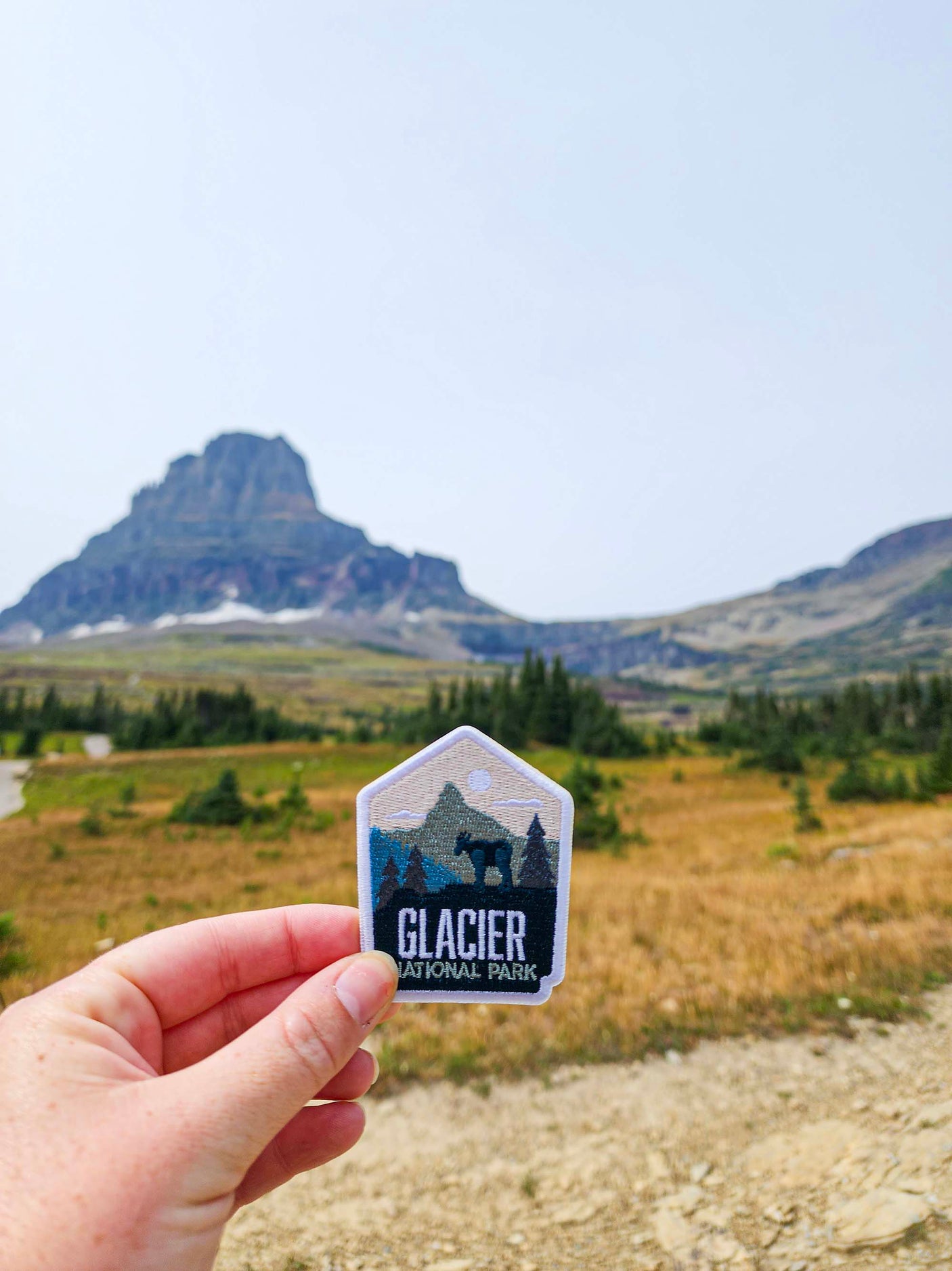 Glacier National Park patch held in hand, featuring mountains and trees with a blue and green color scheme.