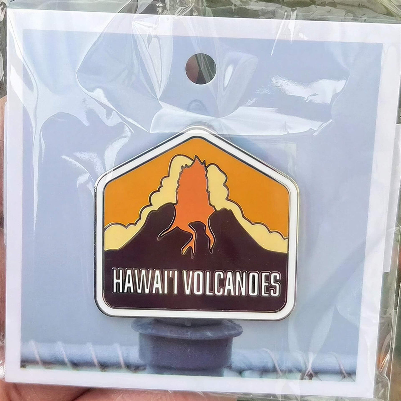 Hawaii Volcanoes National Park enamel pin featuring a volcano silhouette and orange sunset background.