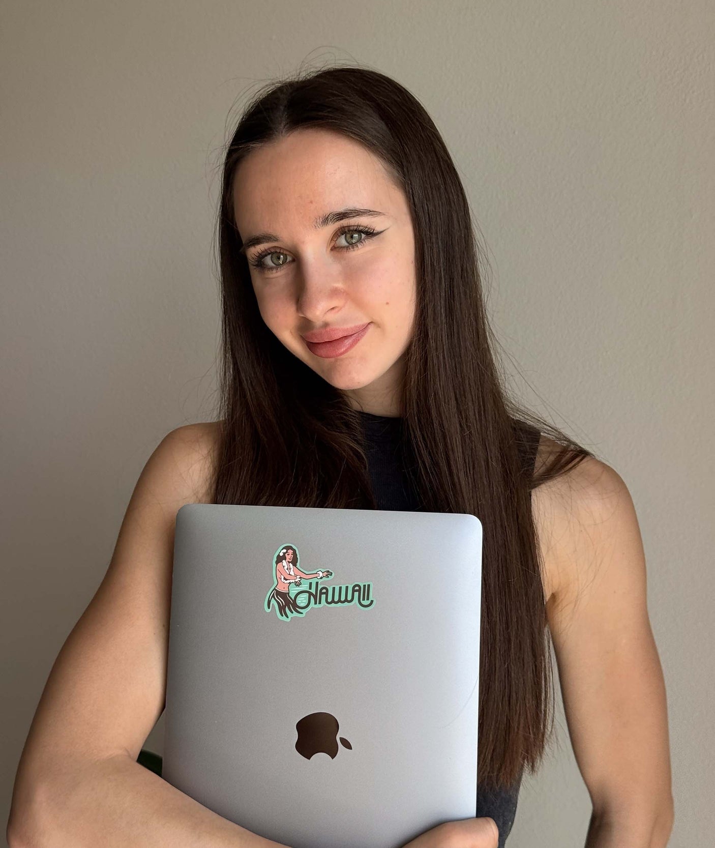 Hawaii hula girl sticker on a silver laptop held by a woman with long dark hair against a plain background.