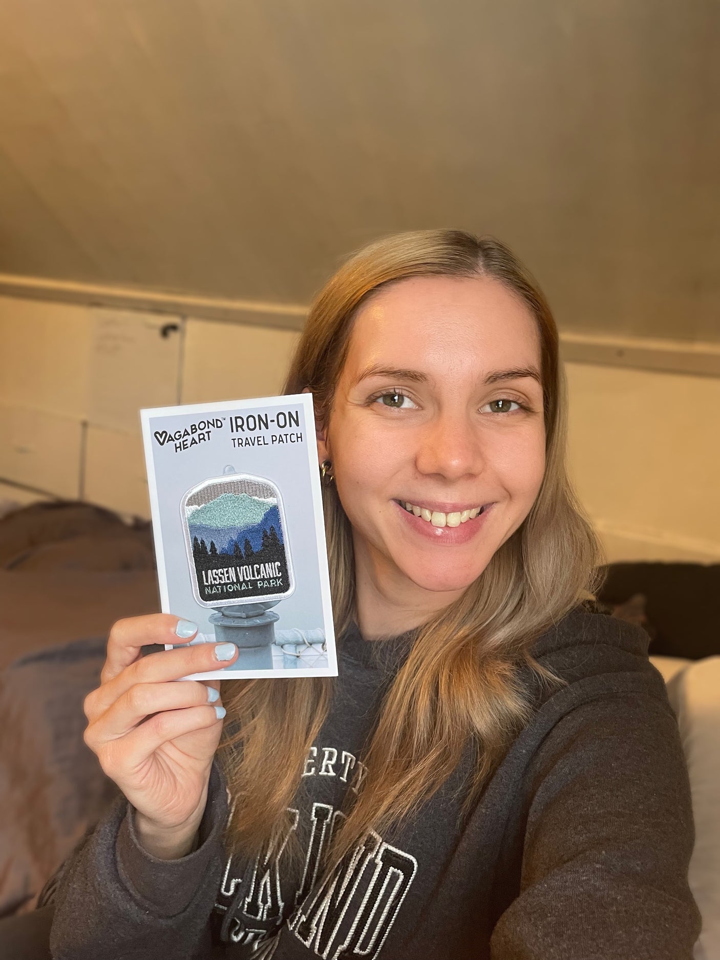 Lassen Volcanic National Park patch held by a smiling woman, featuring mountains and trees in blue and green colors.