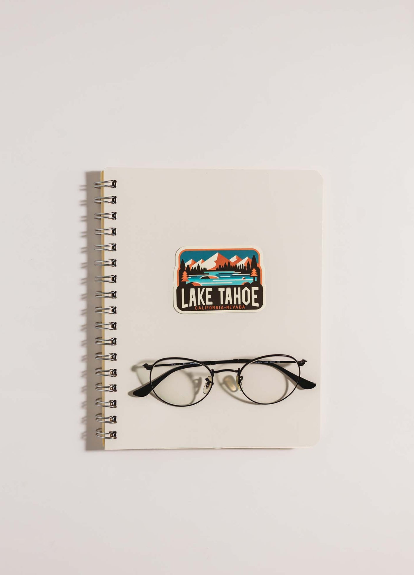 Lake Tahoe sticker featuring mountains and trees, placed on a spiral notebook with round glasses.