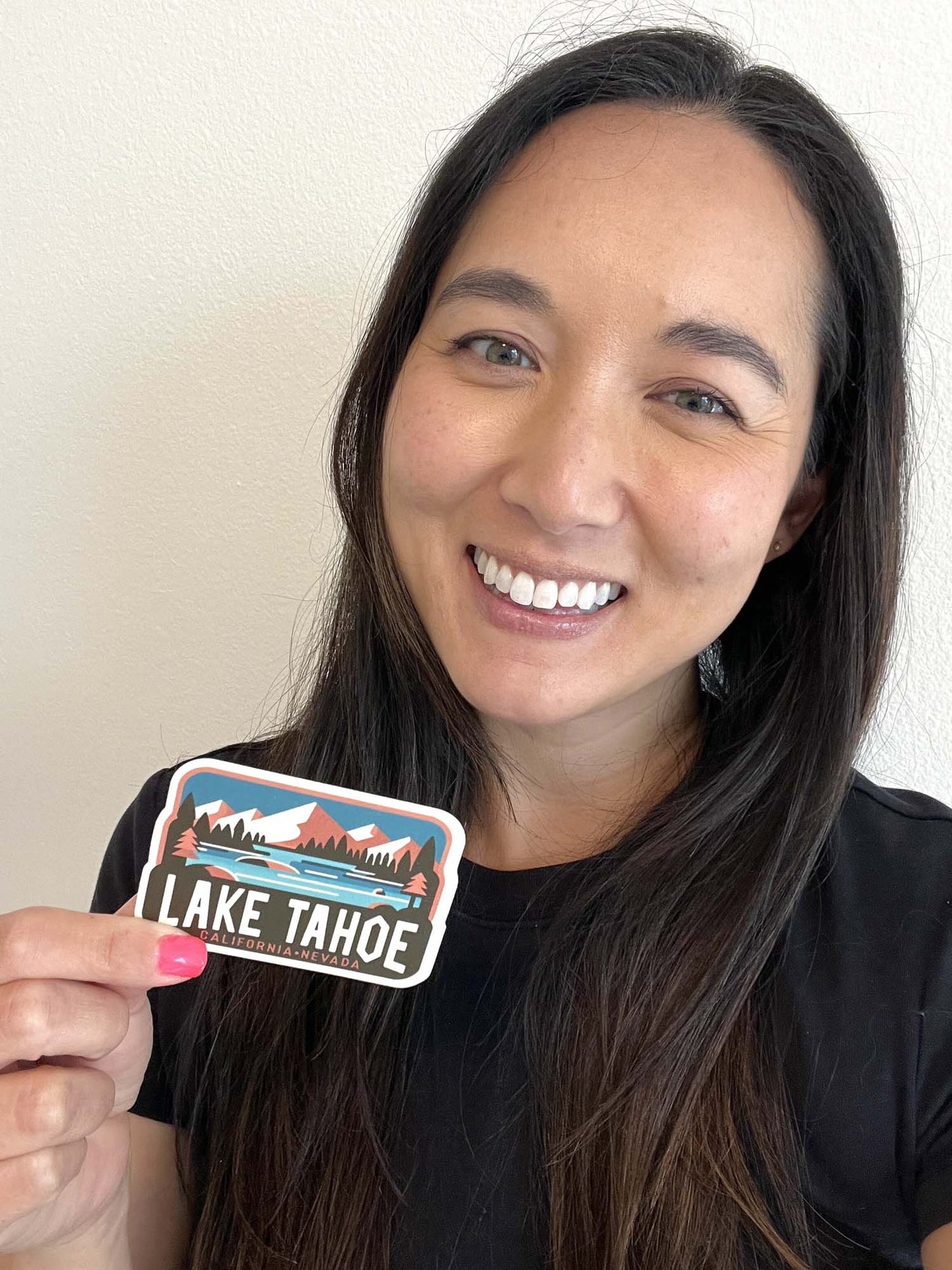 Lake Tahoe sticker held by a person, featuring mountains, trees, and a lake in vibrant colors.