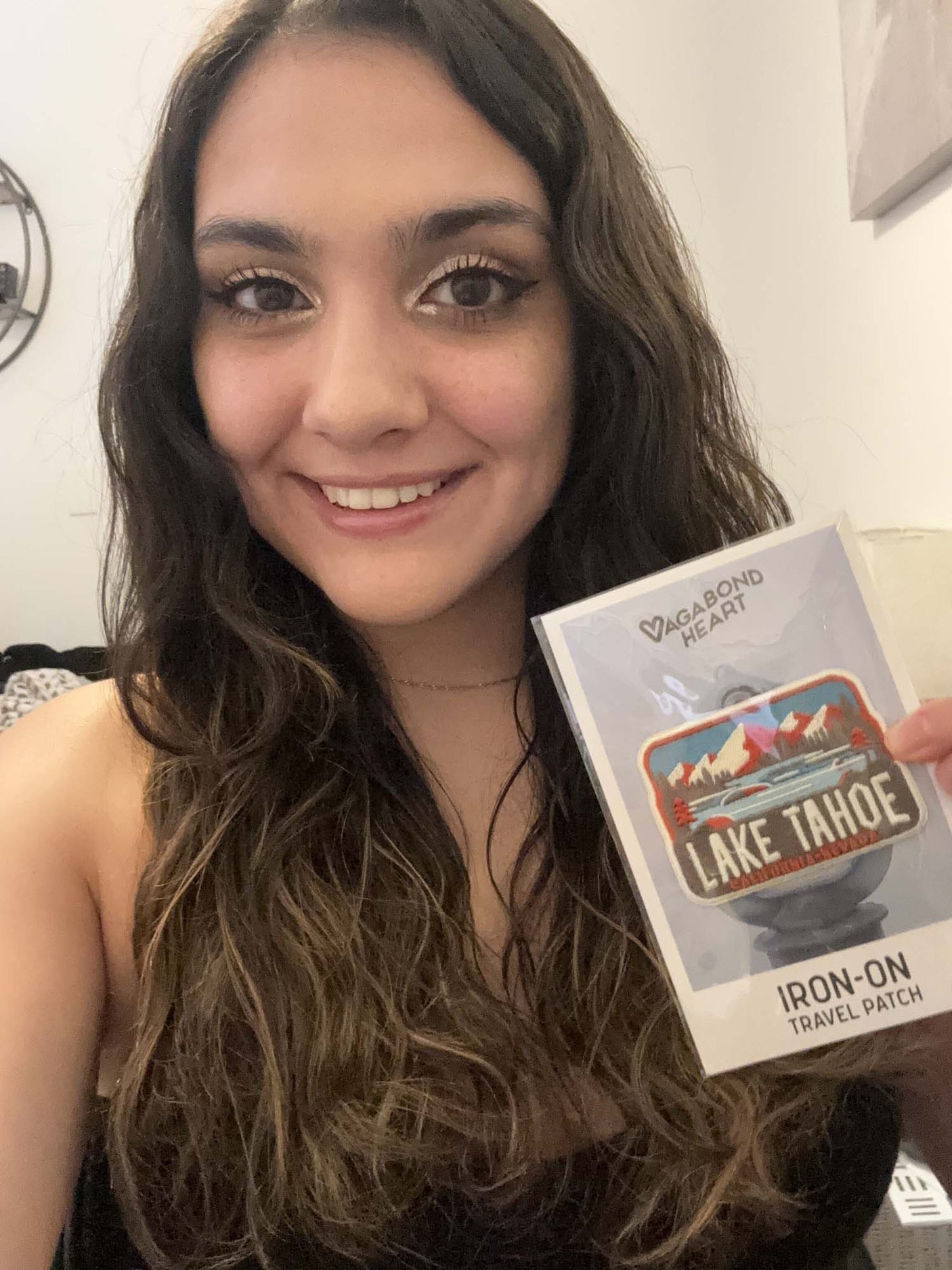 A person holding a Lake Tahoe patch in a clear package, featuring mountains and trees in vibrant colors.