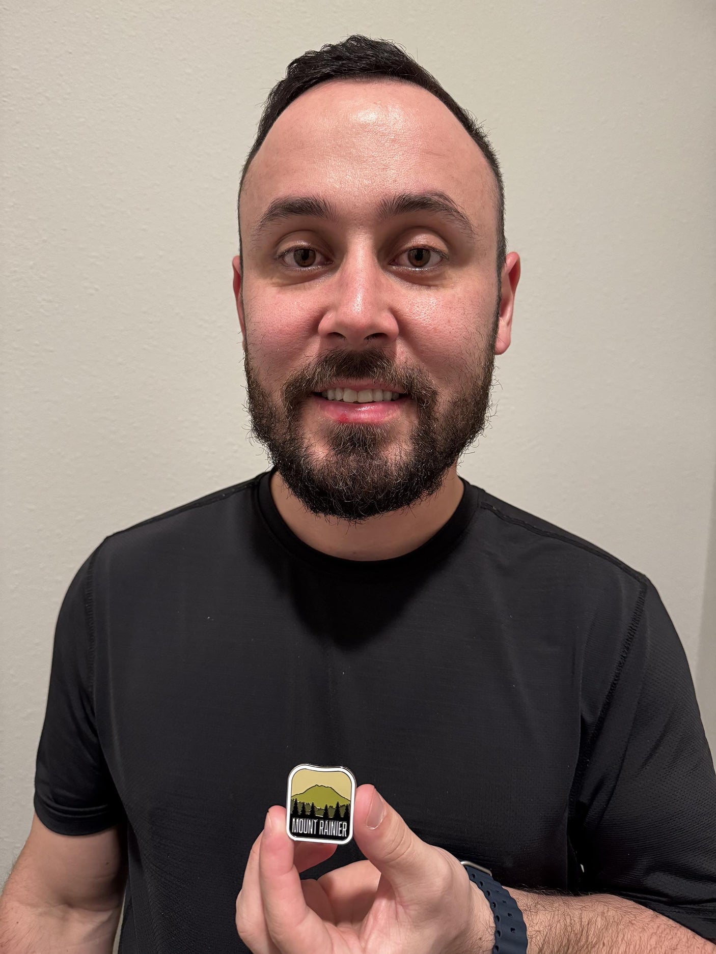 Mount Rainier National Park enamel pin held by a person, featuring a mountain silhouette and "Mount Rainier" text.
