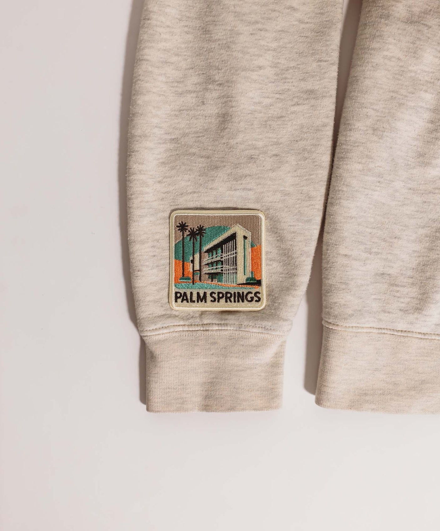 Palm Springs patch featuring a retro building design with palm trees, stitched on a light gray fabric.