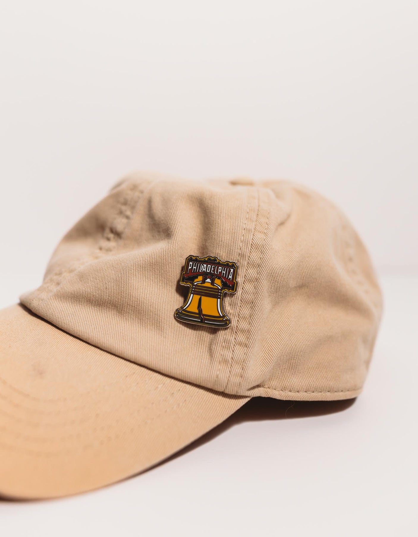 Philadelphia enamel pin featuring the Liberty Bell design, displayed on a beige baseball cap.