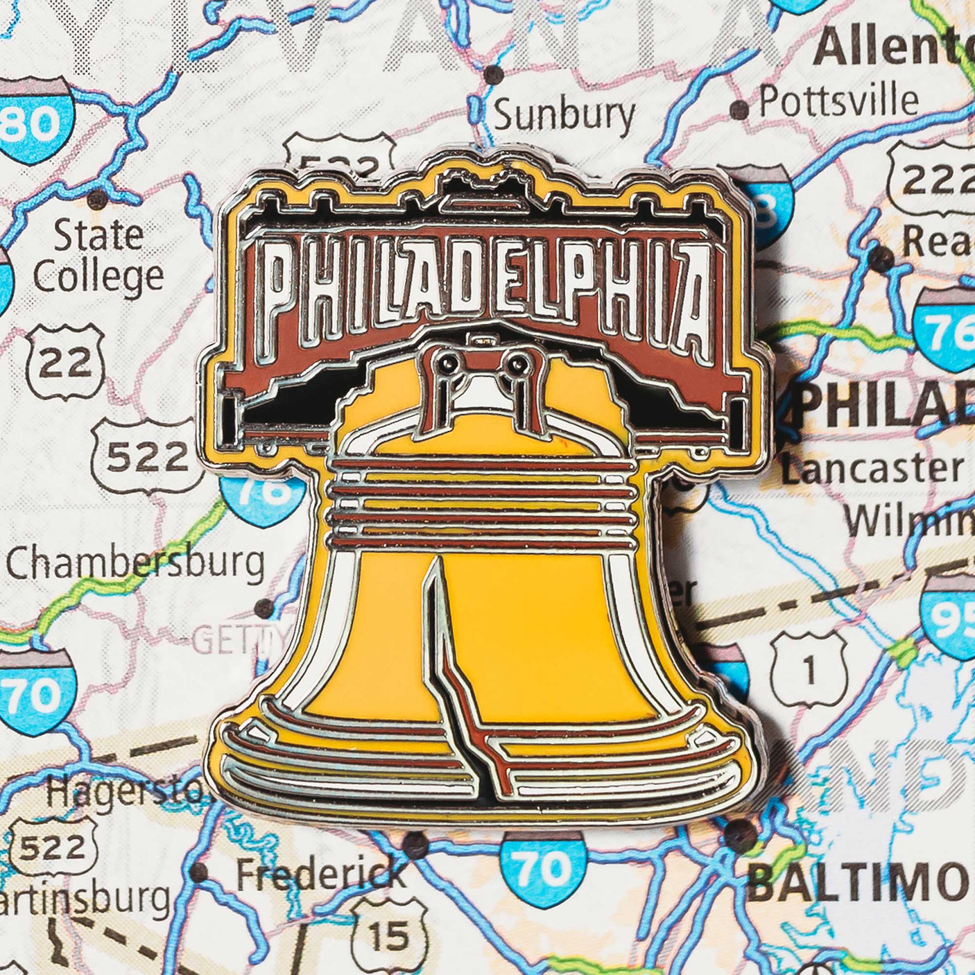 Philadelphia enamel pin featuring the Liberty Bell with a brown and yellow color scheme, set against a map background.