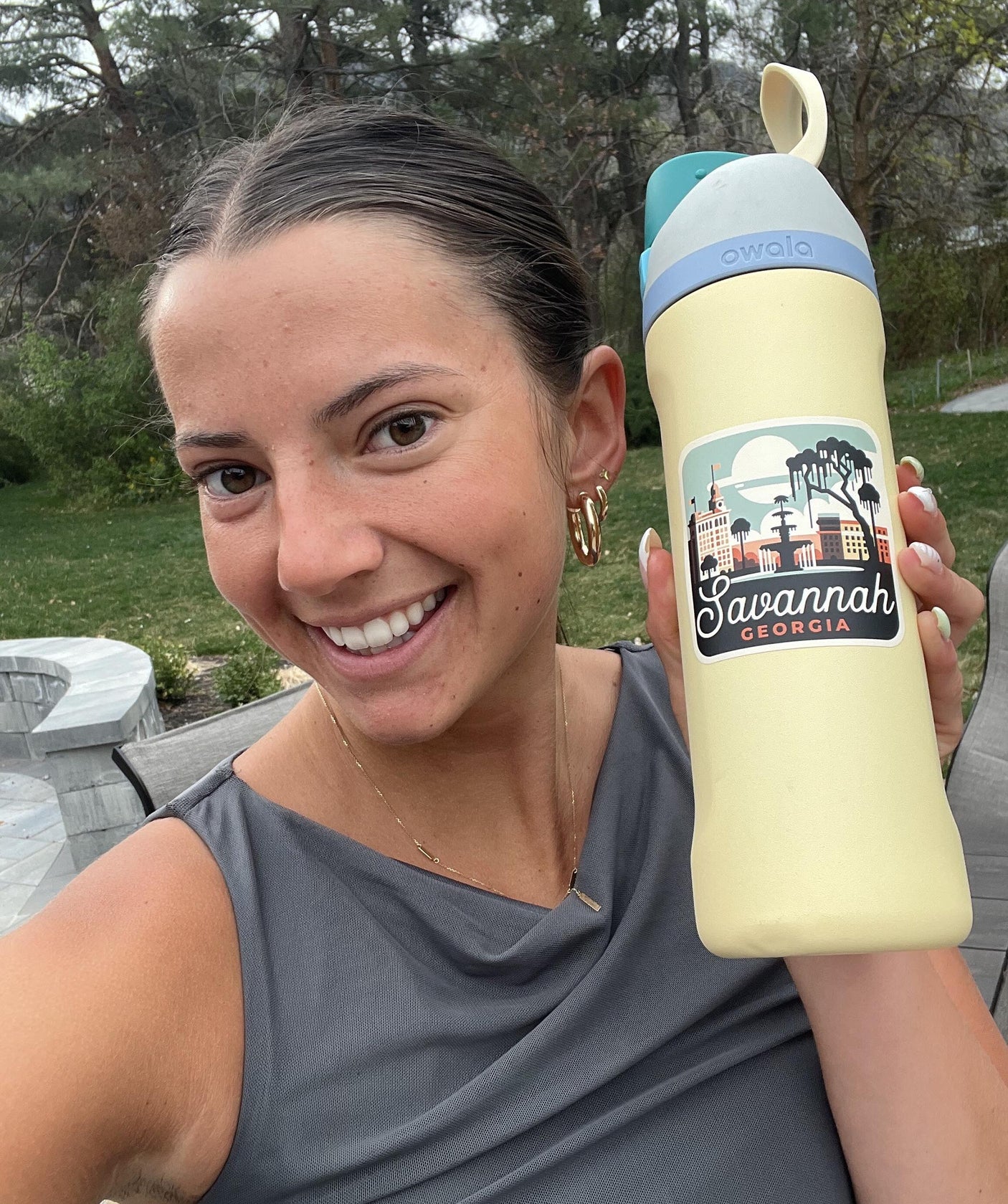 Woman smiling while holding a yellow water bottle featuring a Savannah, Georgia sticker with palm trees and buildings.