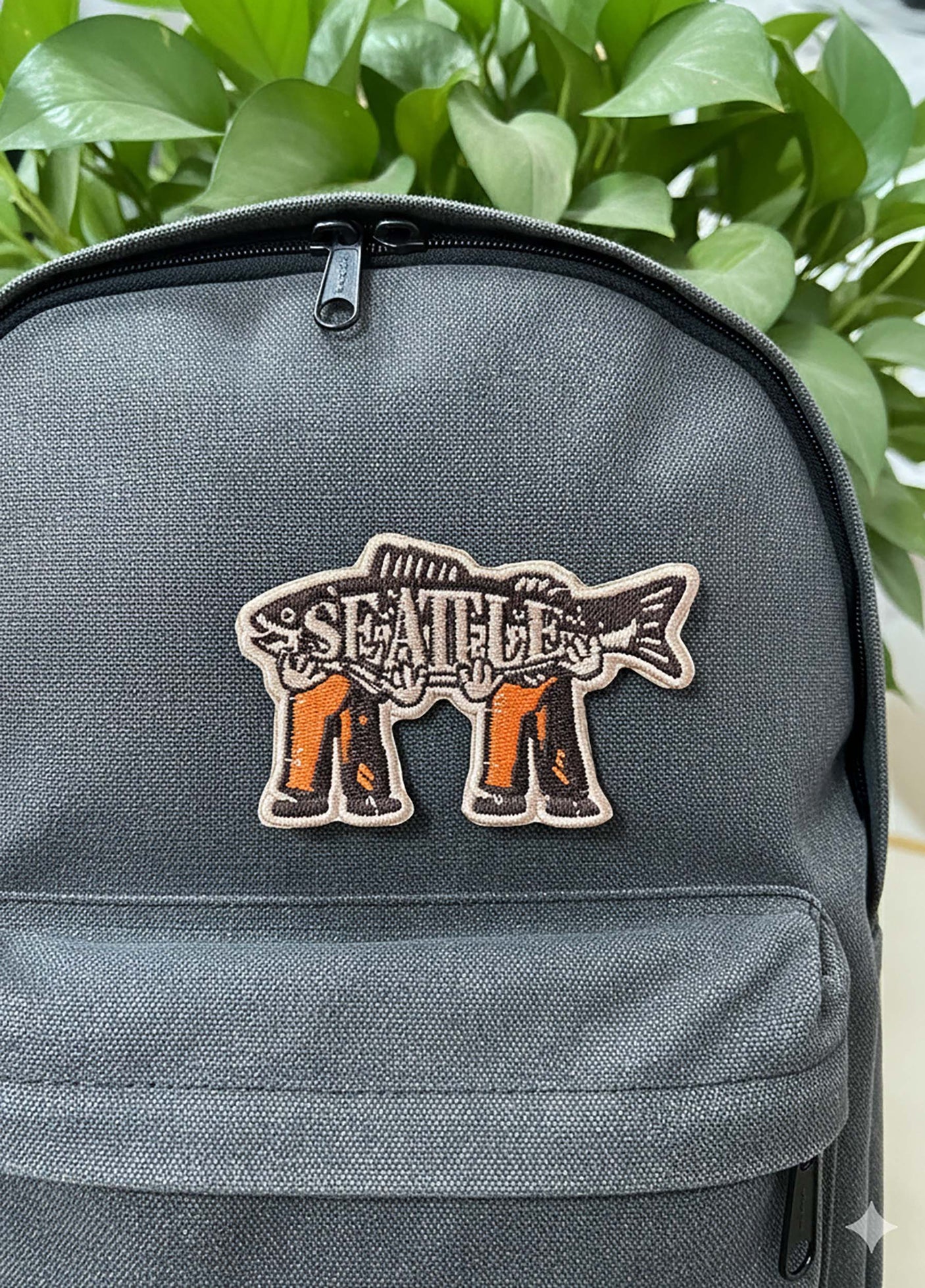 Seattle patch featuring a fish design with orange and black details, attached to a gray backpack.