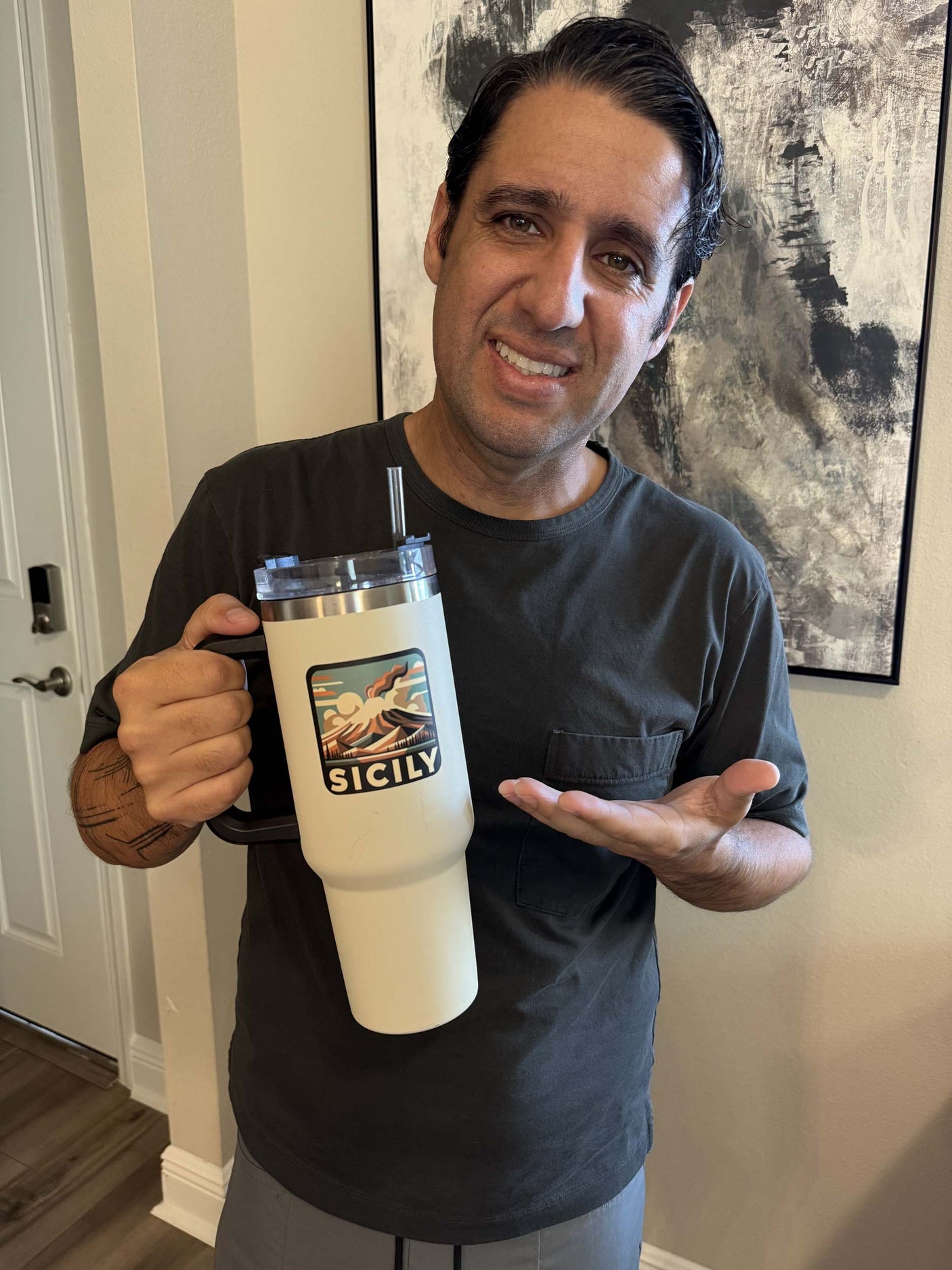A person holding a large white travel mug with a Sicily sticker featuring a landscape design.