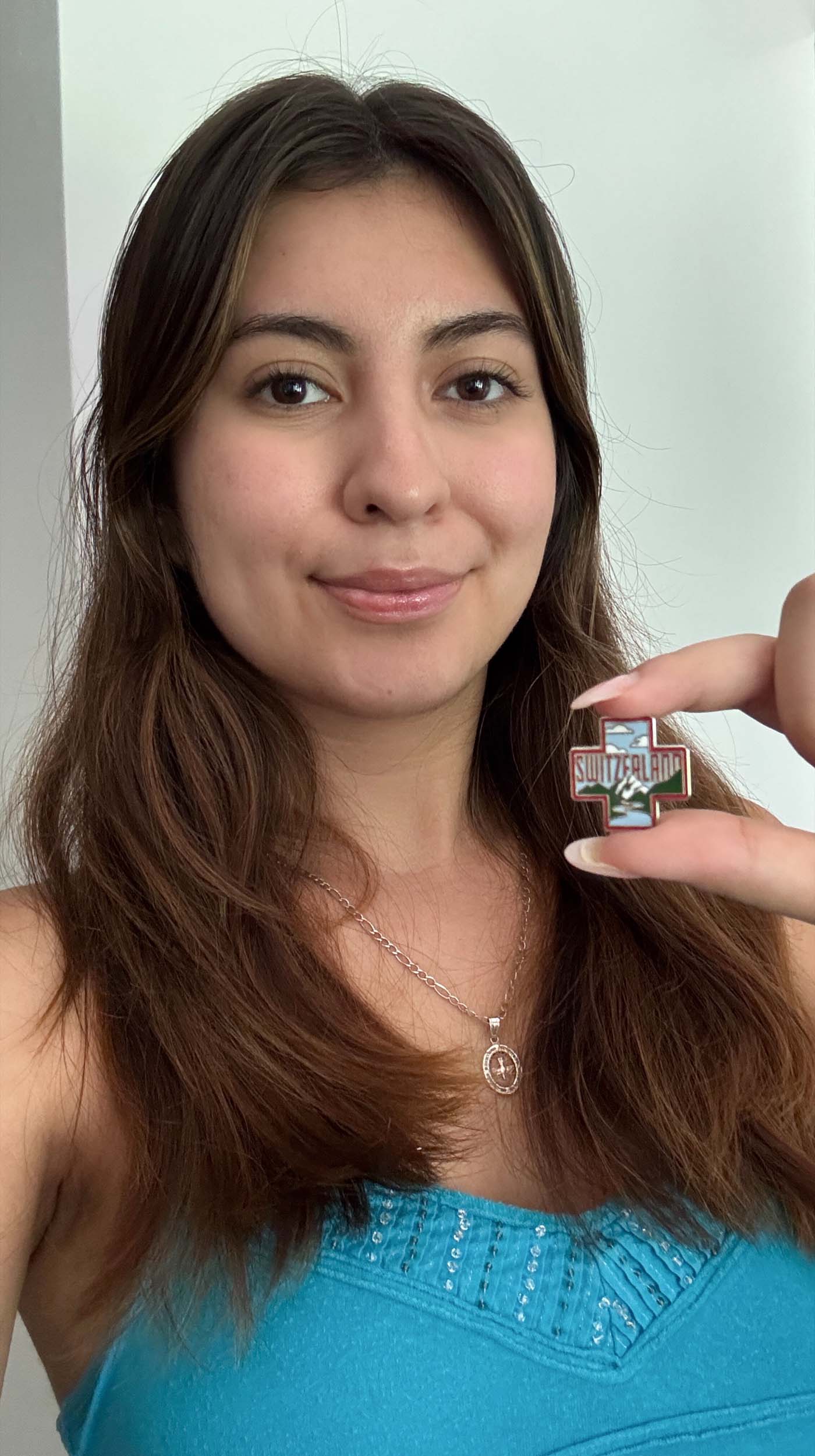 Switzerland enamel pin held by a person with long brown hair, wearing a blue top, against a light background.
