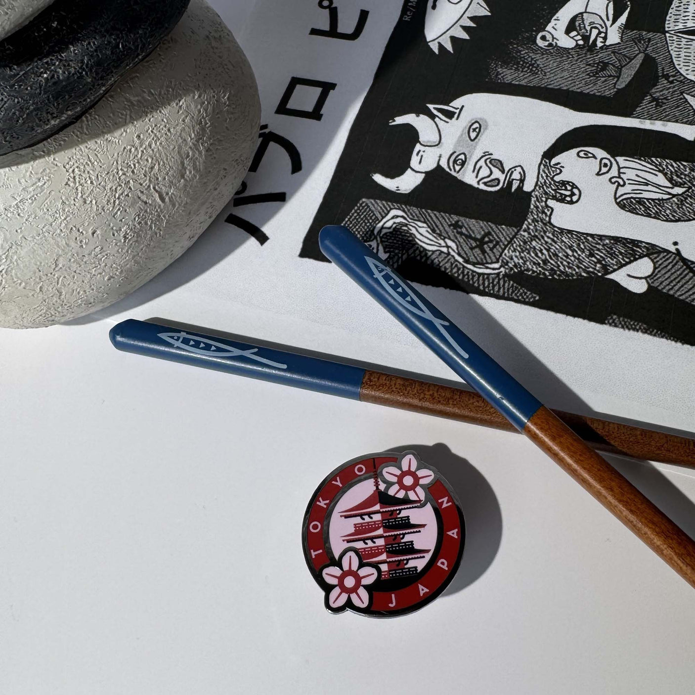 Tokyo Japan enamel pin featuring a pagoda and cherry blossoms, placed beside blue chopsticks and a patterned cloth.
