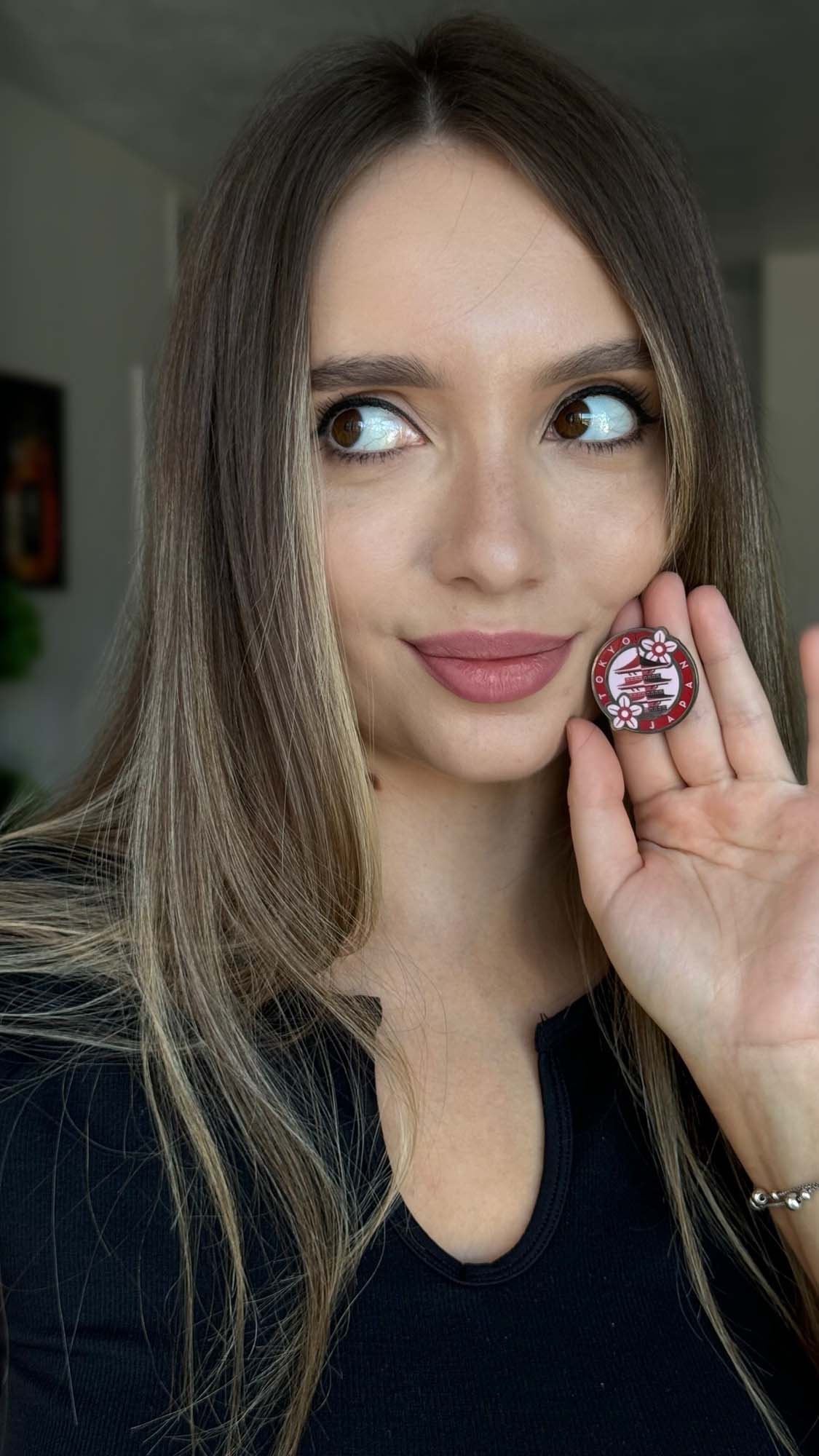 Tokyo Japan enamel pin held by a woman with long hair, wearing a black top, showcasing the pin's red and white design.