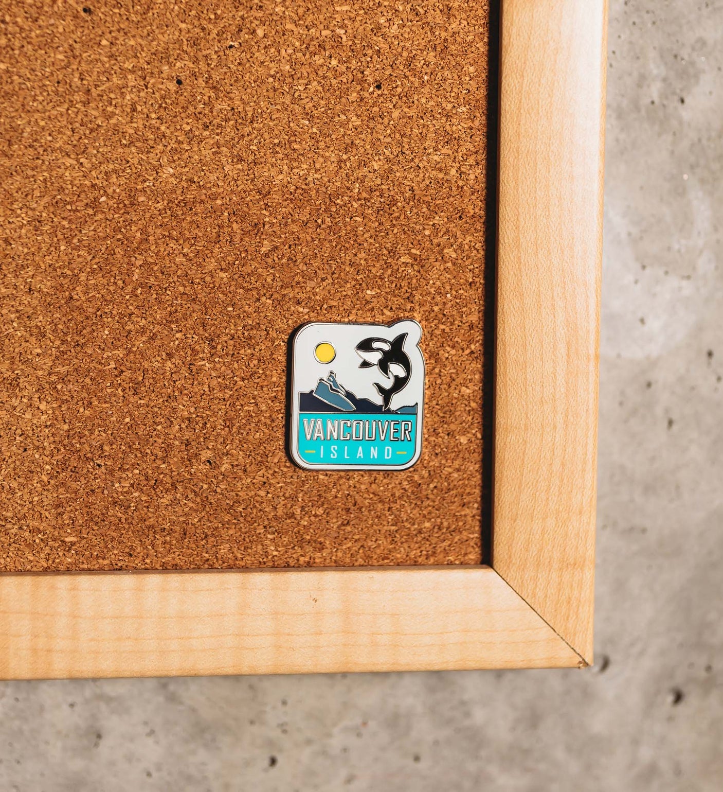 Vancouver Island enamel pin featuring a black orca and blue text on a corkboard background.