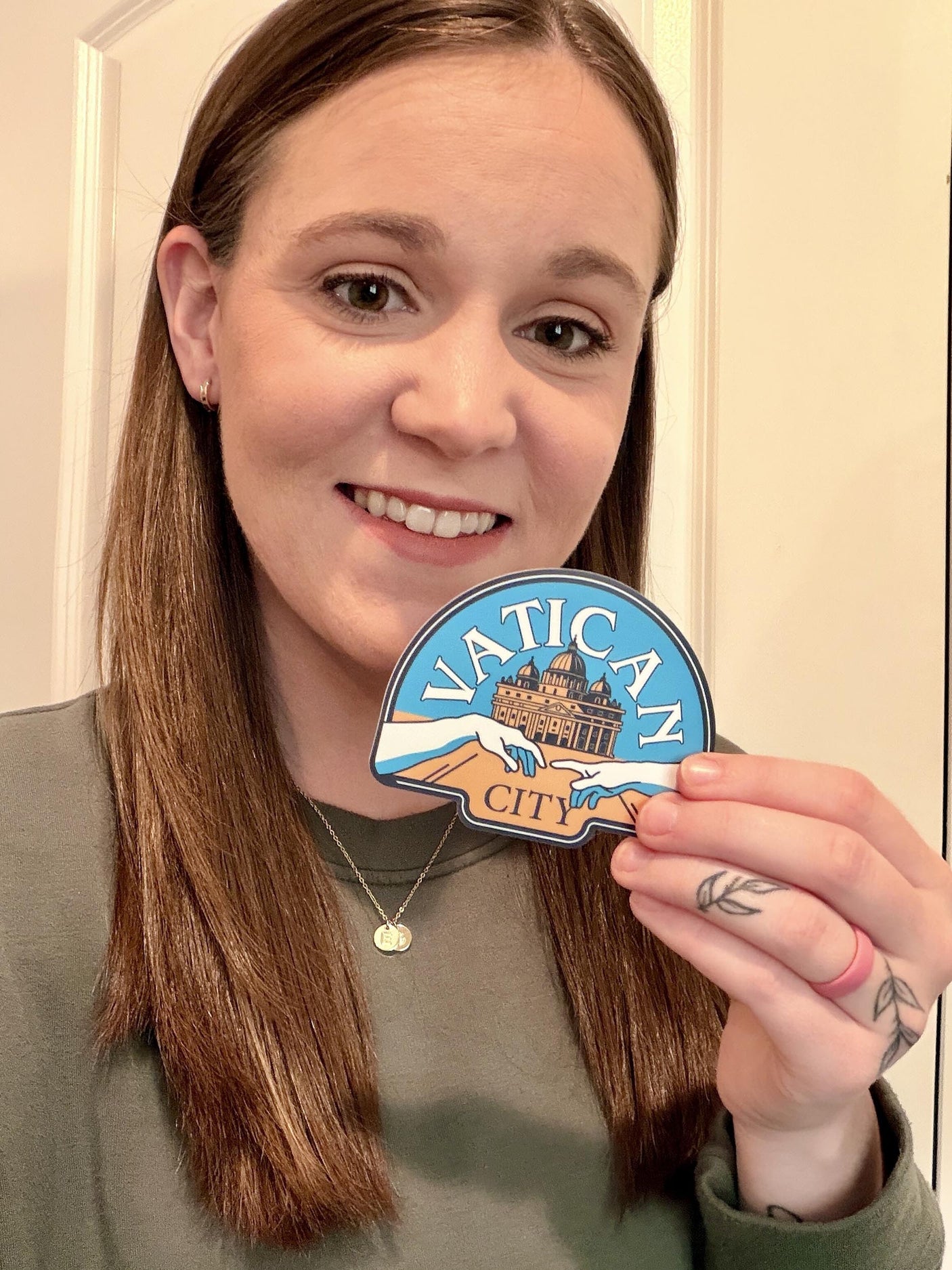 Vatican City sticker held by a person with long brown hair, wearing a green top, against a light background.