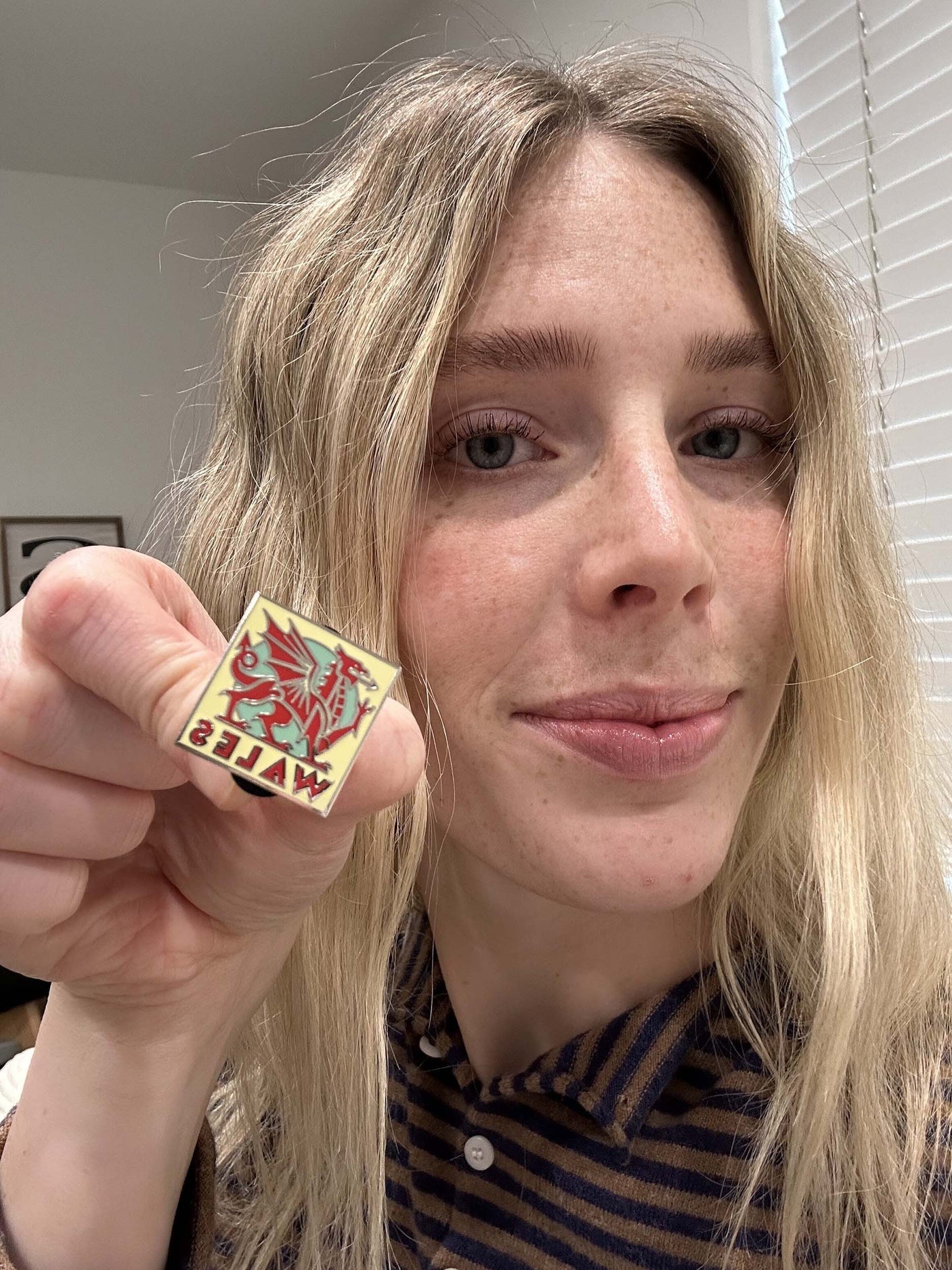 Wales enamel pin held by a person, featuring a red dragon design and the word "Wales" in bold letters.