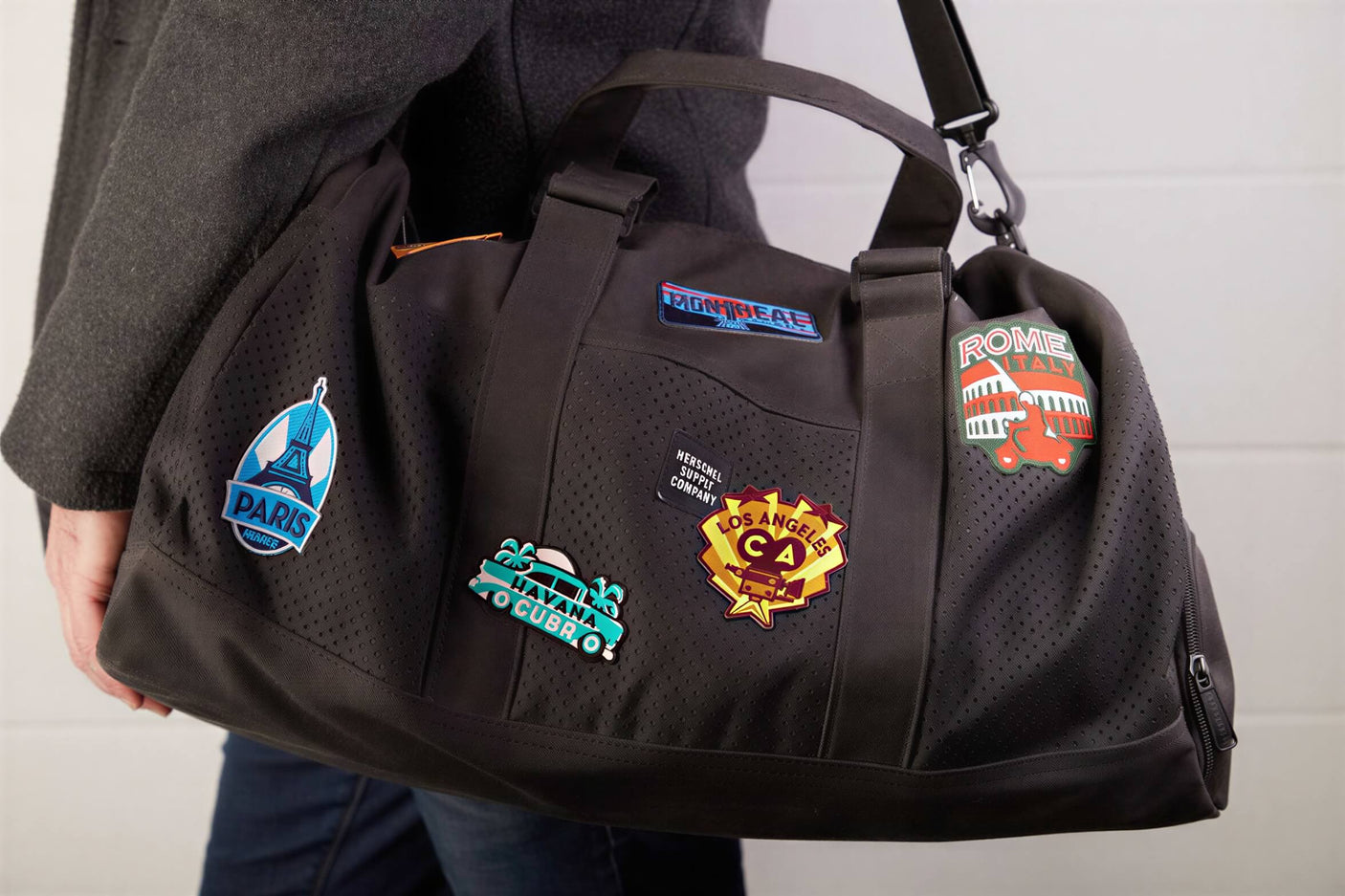 Taj Mahal patch on a black duffel bag, featuring colorful travel-themed patches from various cities.