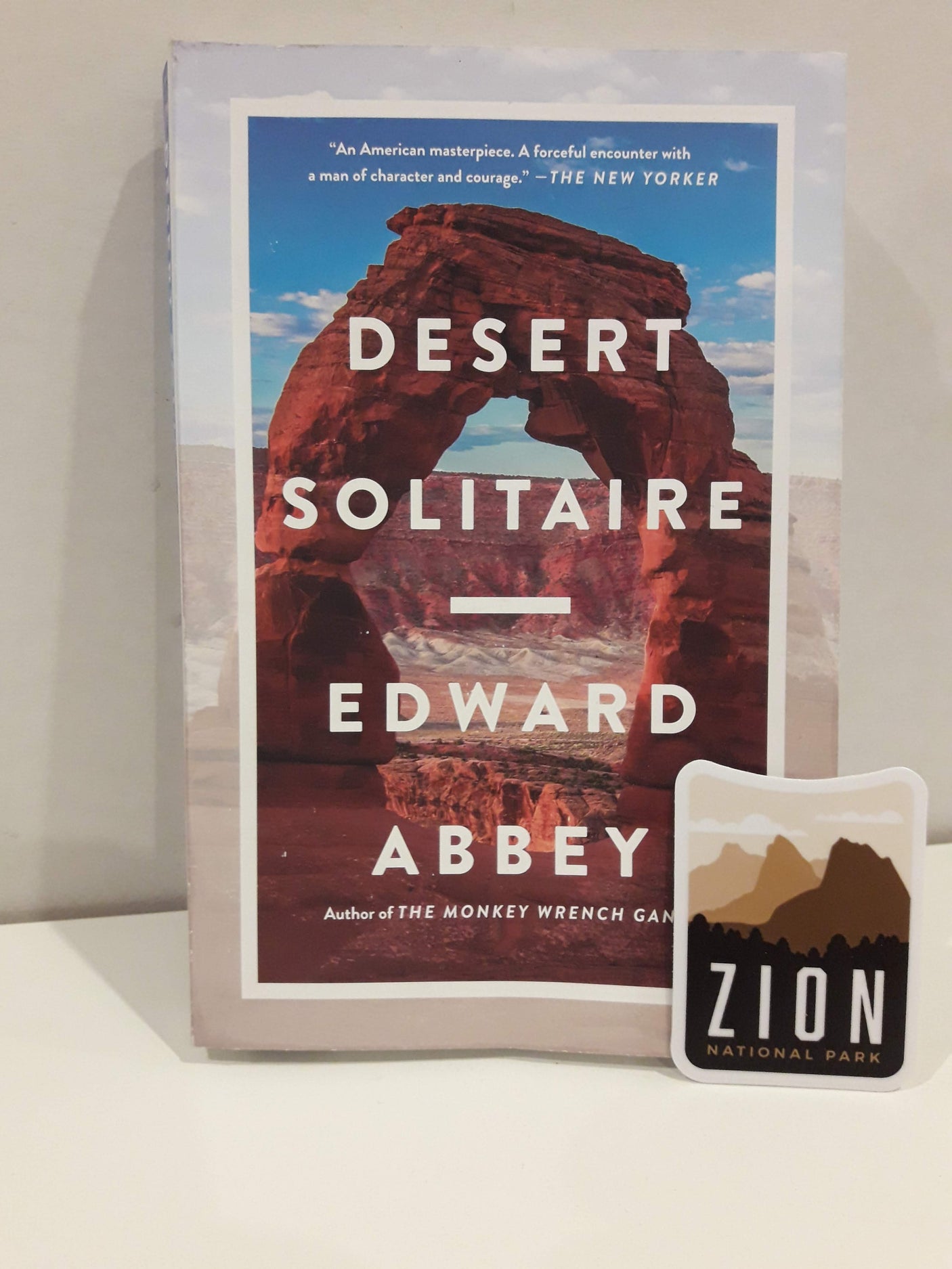 Zion National Park sticker displayed next to the book "Desert Solitaire" by Edward Abbey on a white surface.