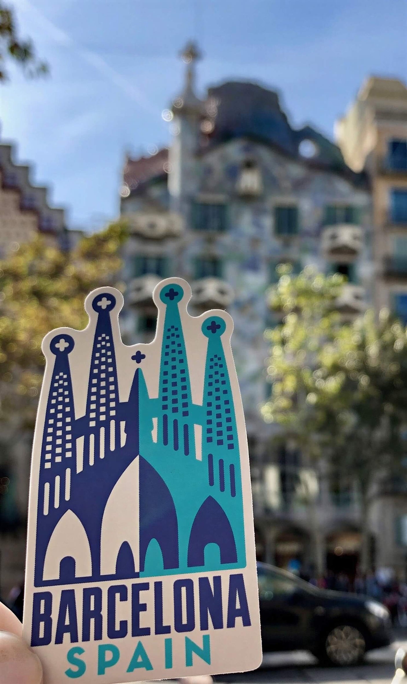 Barcelona Spain sticker featuring iconic architecture with blue and white colors, held in front of a colorful building.