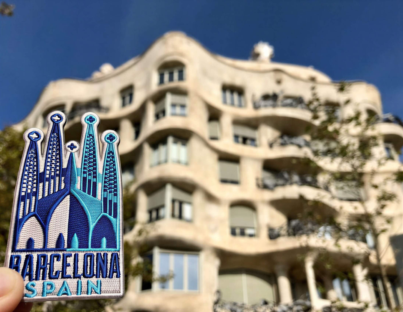 Barcelona Spain patch featuring blue and white colors, held in front of a modern architectural building.
