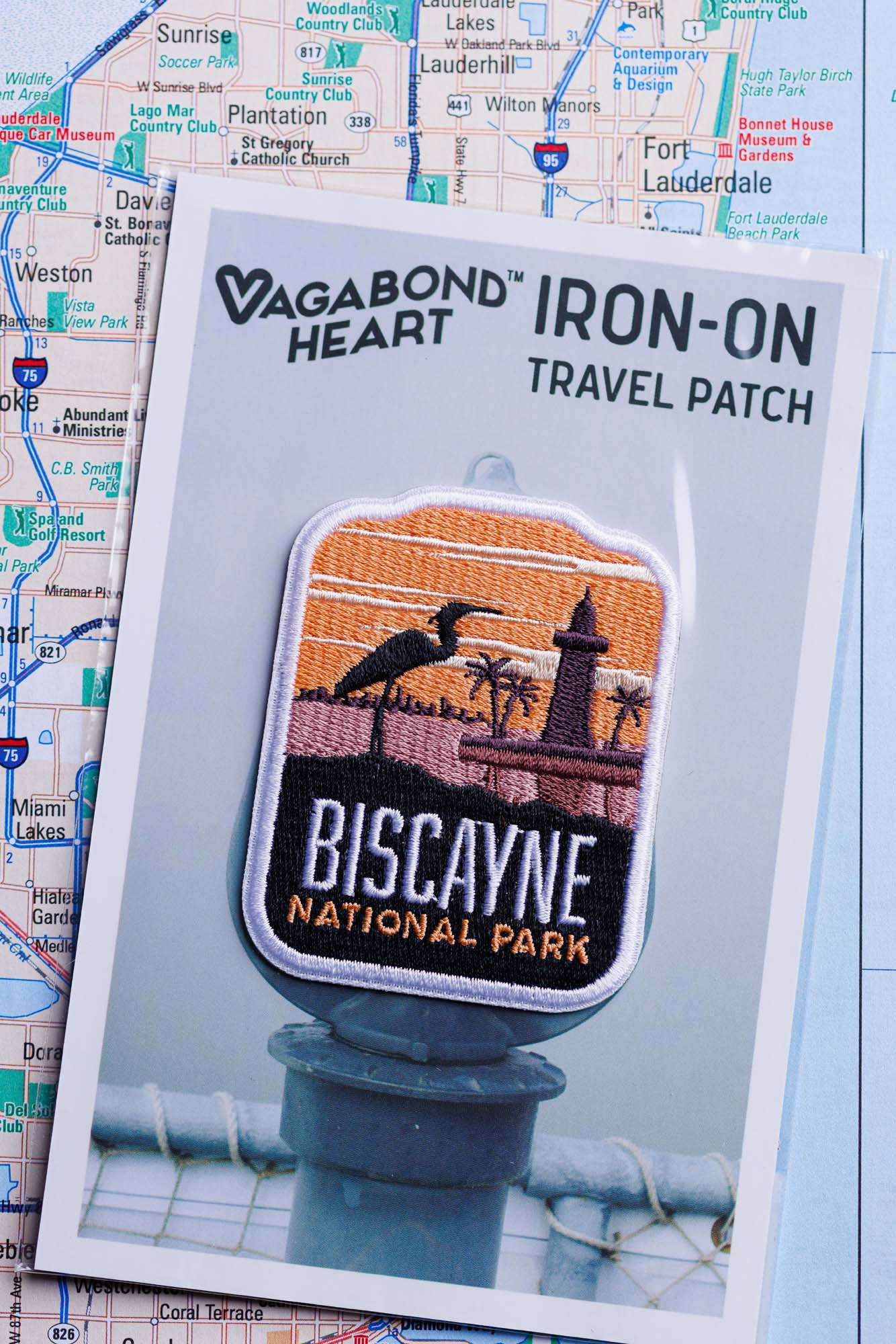 Biscayne National Park patch featuring a lighthouse, palm trees, and an orange sunset on a backing card.