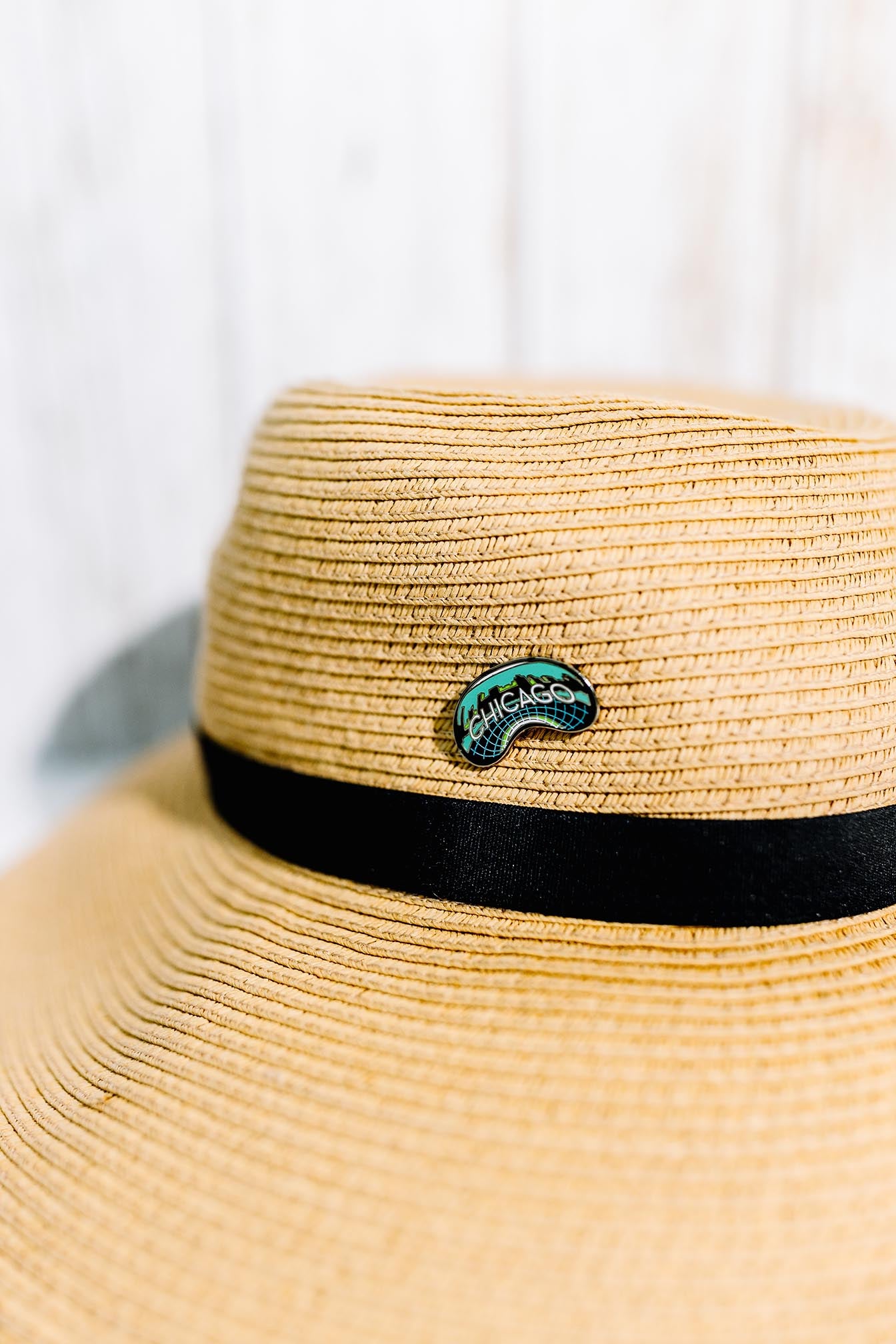 Chicago enamel pin displayed on a tan straw hat with a black band.