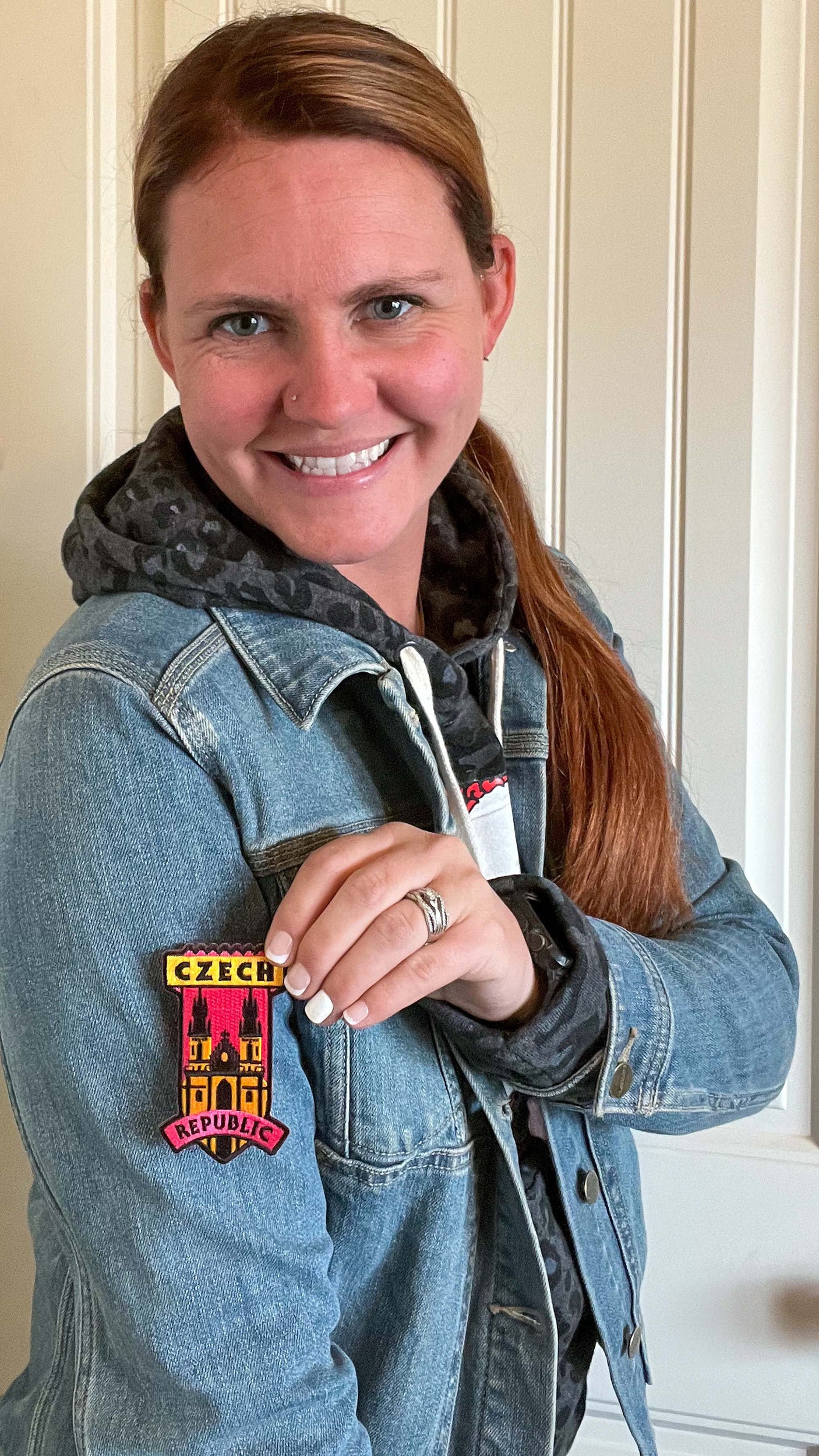 Czech Republic patch in red, yellow, and black on a denim jacket sleeve, worn by a woman with long brown hair.