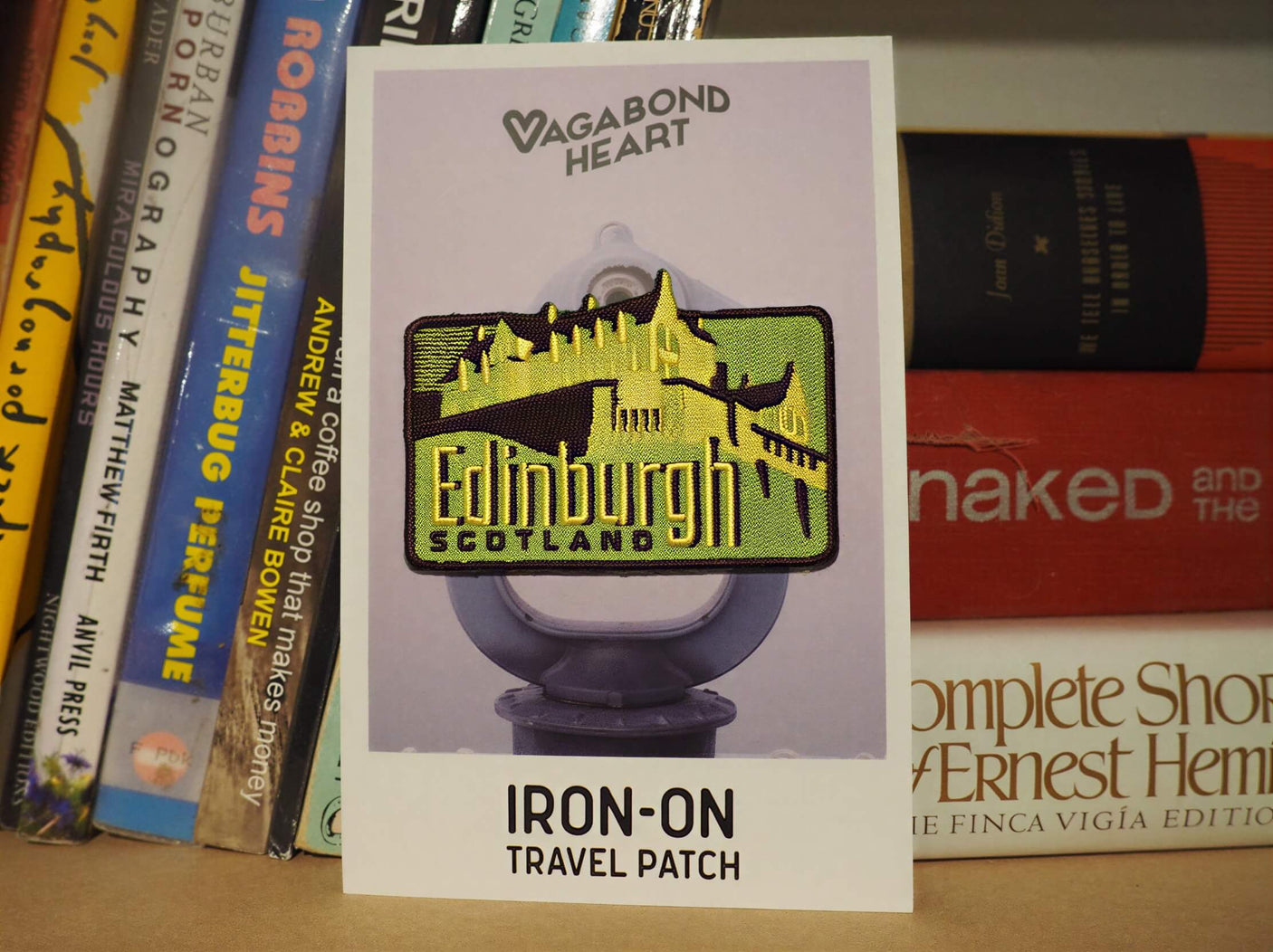 Edinburgh Scotland iron-on patch featuring a castle design on a backing card, displayed among books.