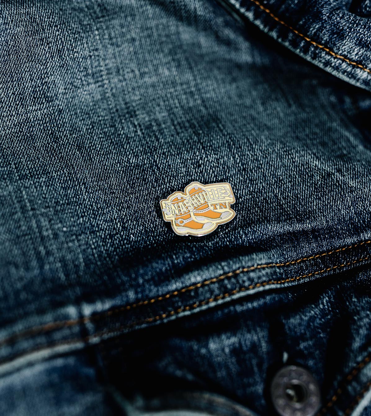 Nashville Tennessee enamel pin featuring orange and white design on a denim jacket.