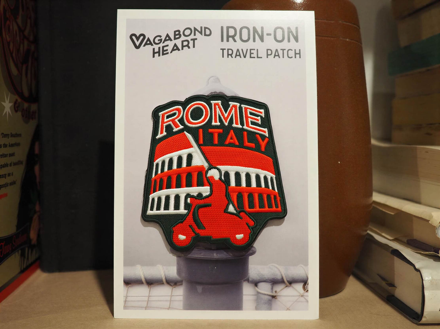 Rome Italy iron-on travel patch featuring a red and black design with the Colosseum and a scooter on a backing card.