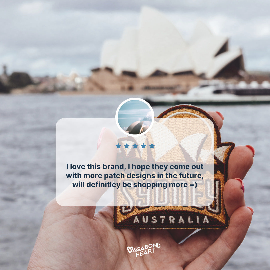 Sydney Australia patch featuring a tan background with white lettering, held in hand against a blurred waterfront scene.