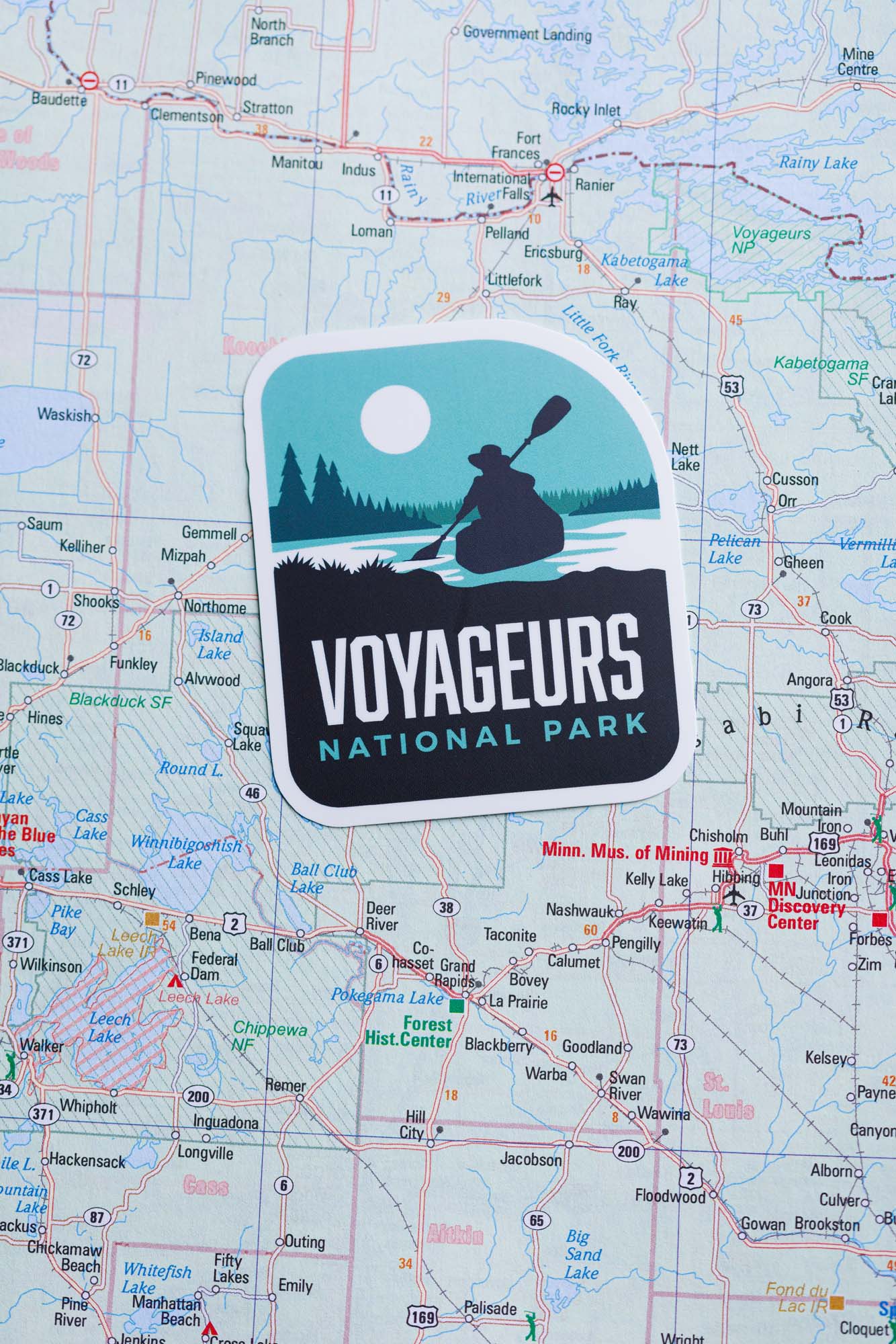 Voyageurs National Park sticker featuring a silhouette of a kayaker on a blue and green background, placed on a map.