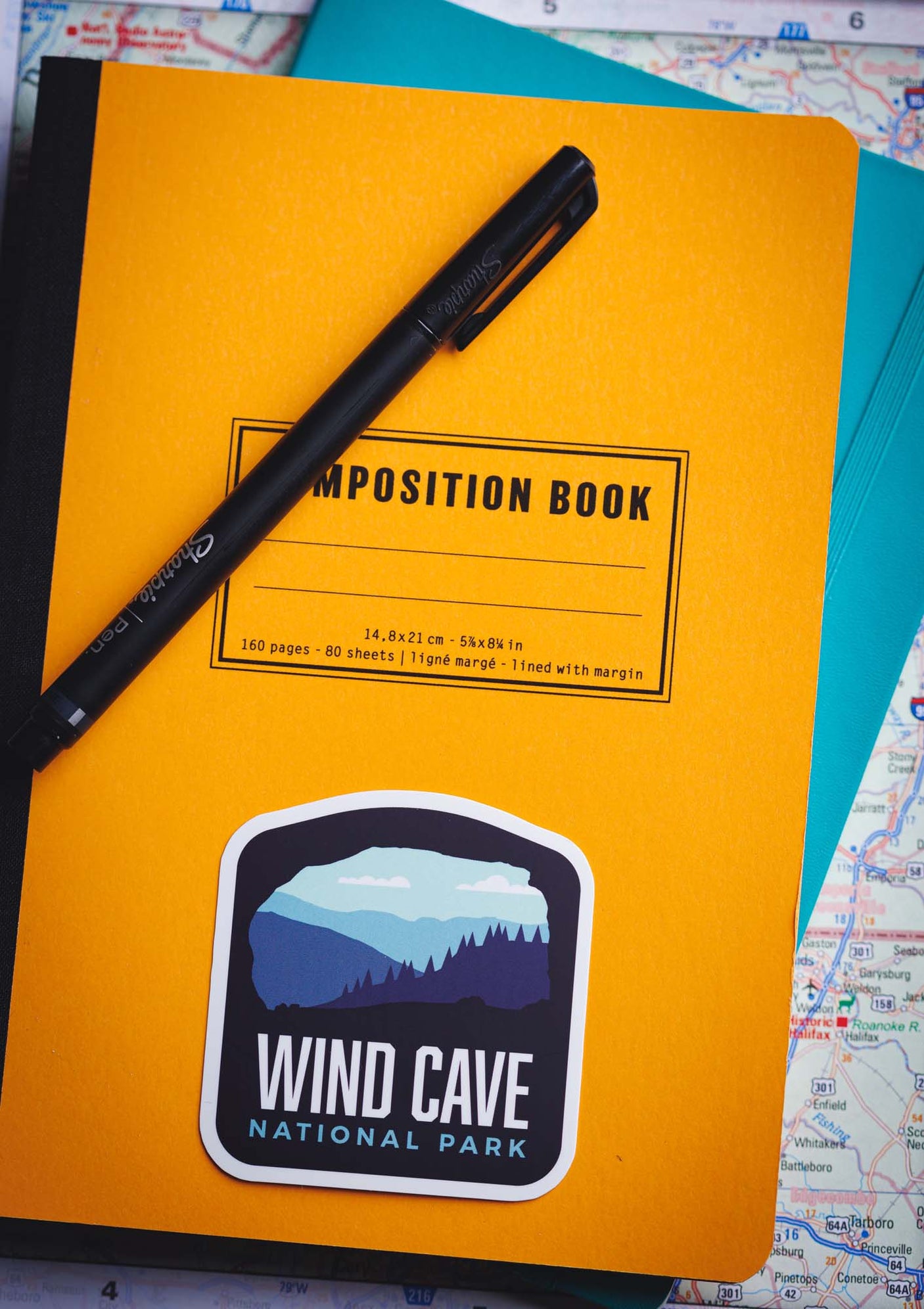 Wind Cave National Park sticker on a yellow composition notebook with a black pen and a map in the background.