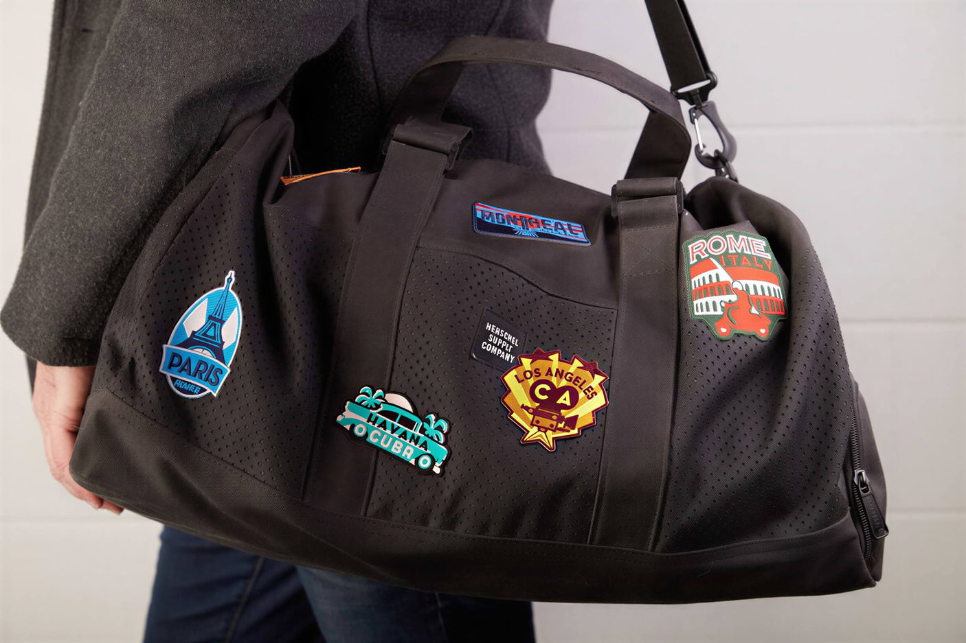 Spain patch on a black duffel bag, alongside other travel patches from various cities.