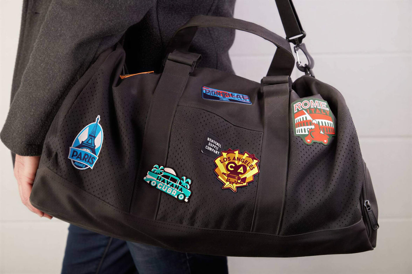 Switzerland patch on a black duffel bag, alongside other travel patches from various cities.