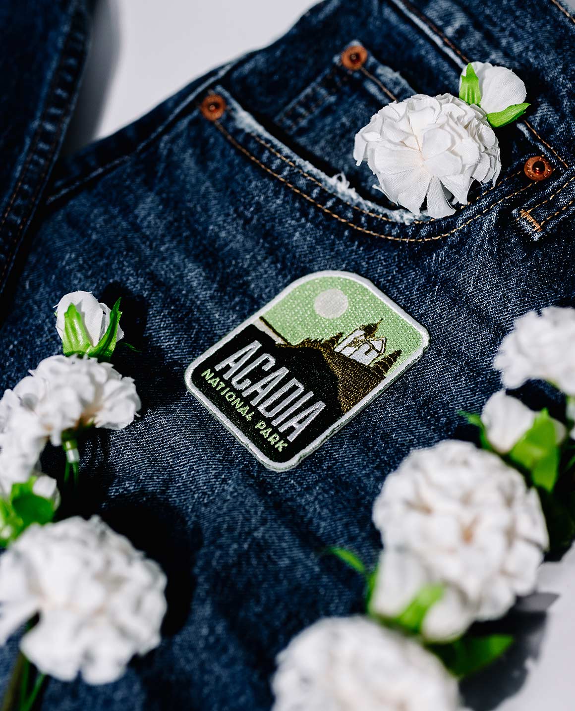 Key West Florida patch on dark denim jeans, surrounded by white flowers.