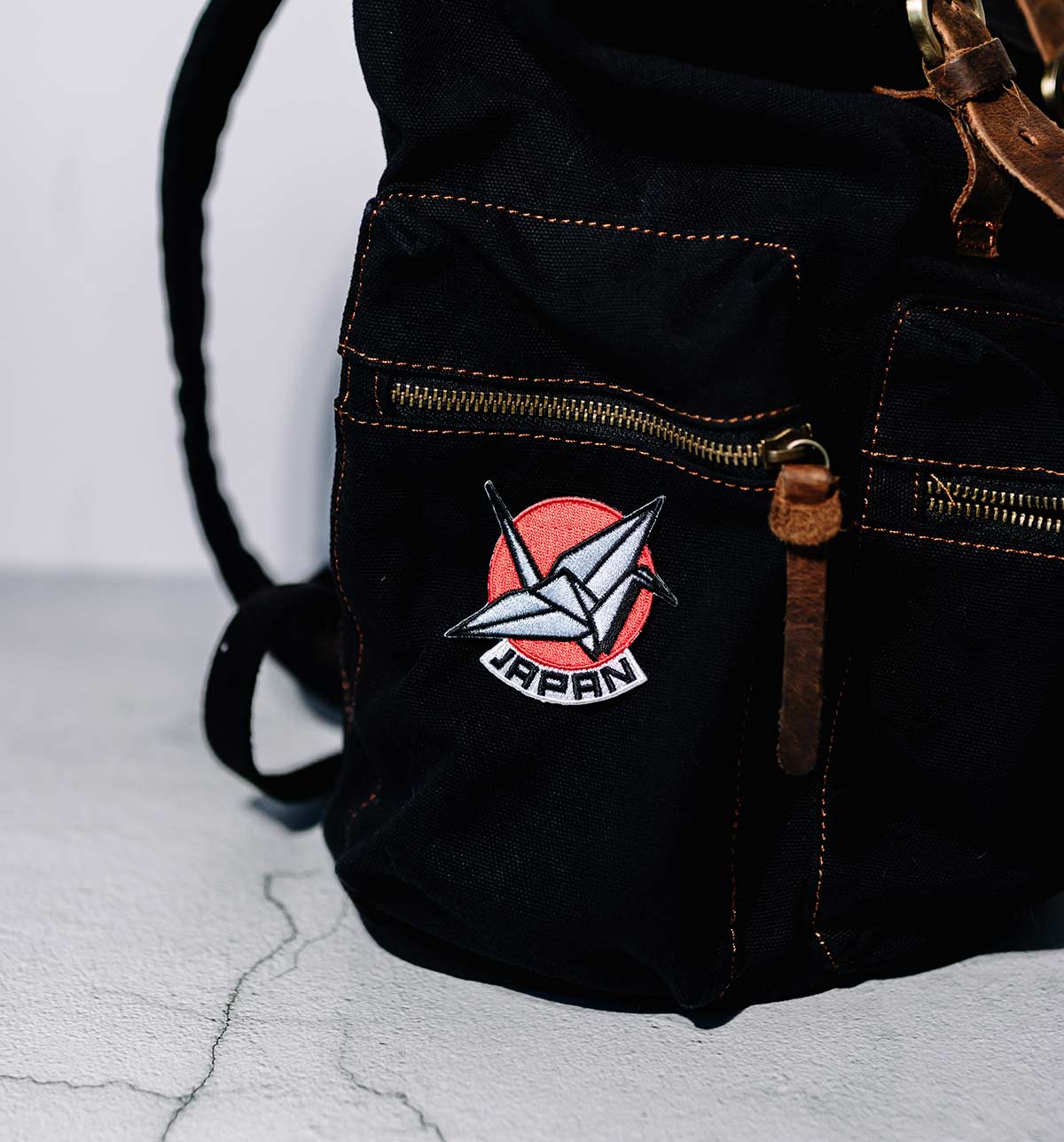 Portland Oregon patch featuring a red circle and white crane design, attached to a black bag with zippers.