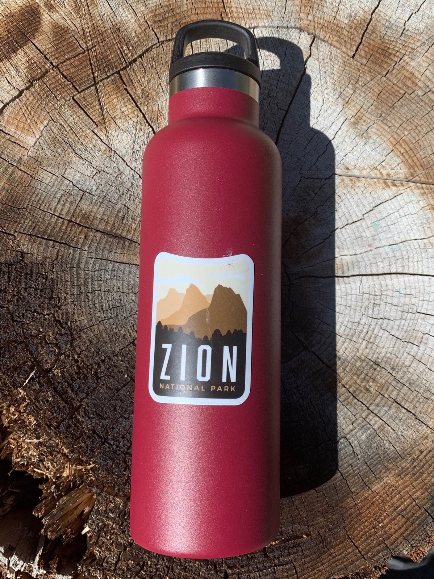 Zion National Park sticker on a red water bottle, featuring mountain graphics and text in black and white.