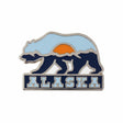 Alaska enamel pin featuring a bear silhouette, mountains, and a sunset in blue, orange, and white colors.