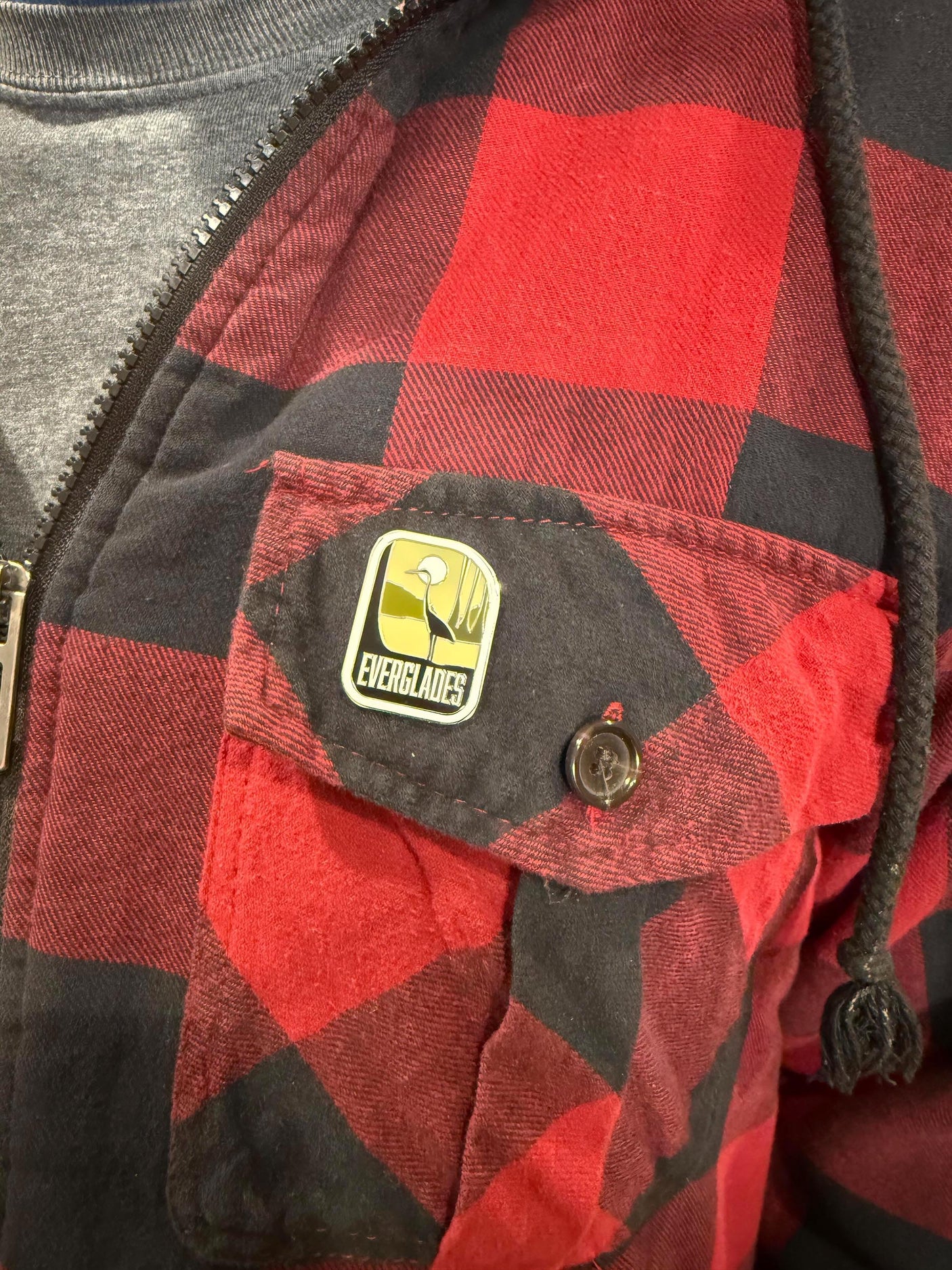 Everglades National Park enamel pin displayed on a red and black checkered shirt.