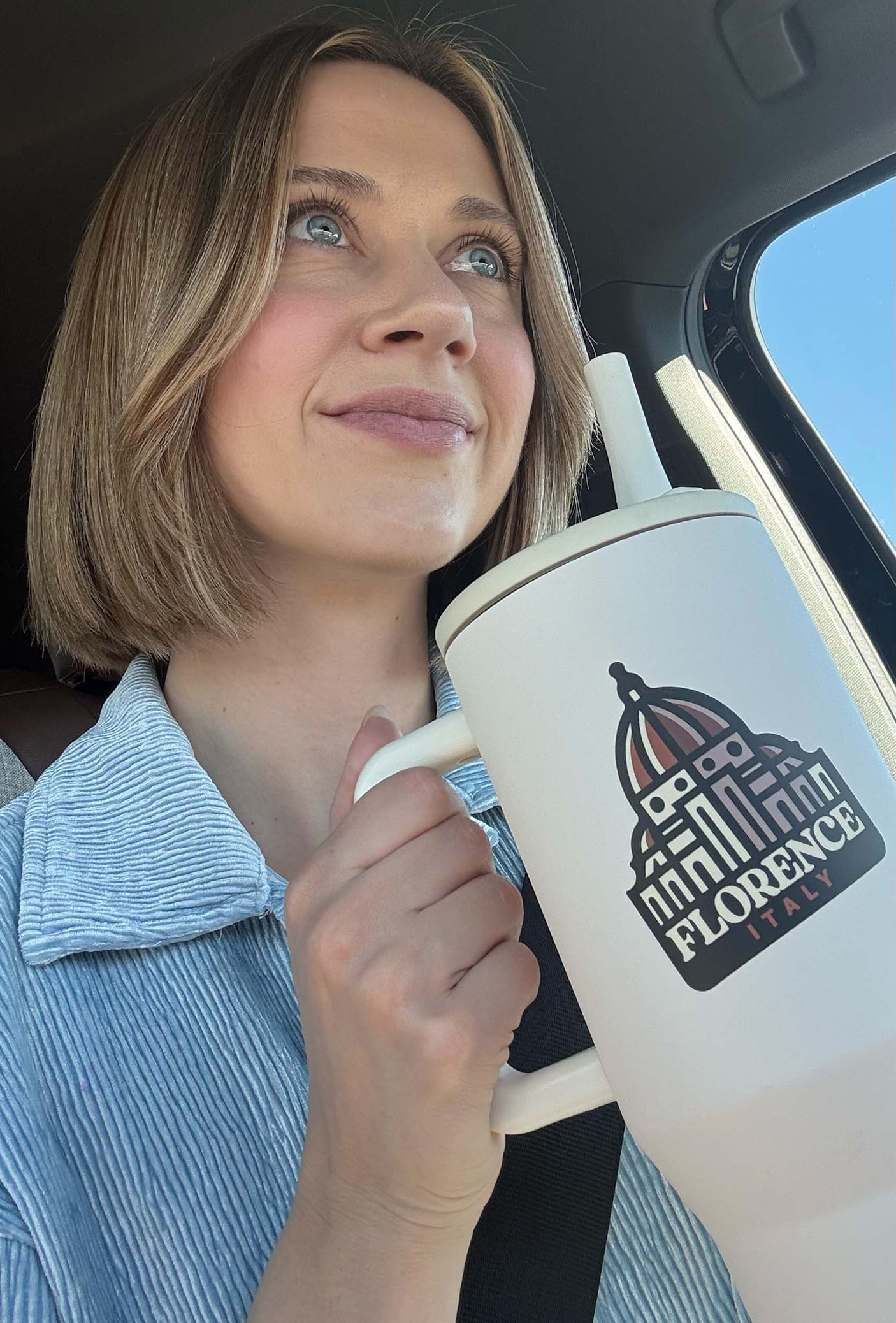 Woman in a car holding a white tumbler featuring a Florence Italy sticker with a dome design.