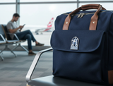 Greece enamel pin featuring a blue and white design, displayed on a navy bag in an airport setting.