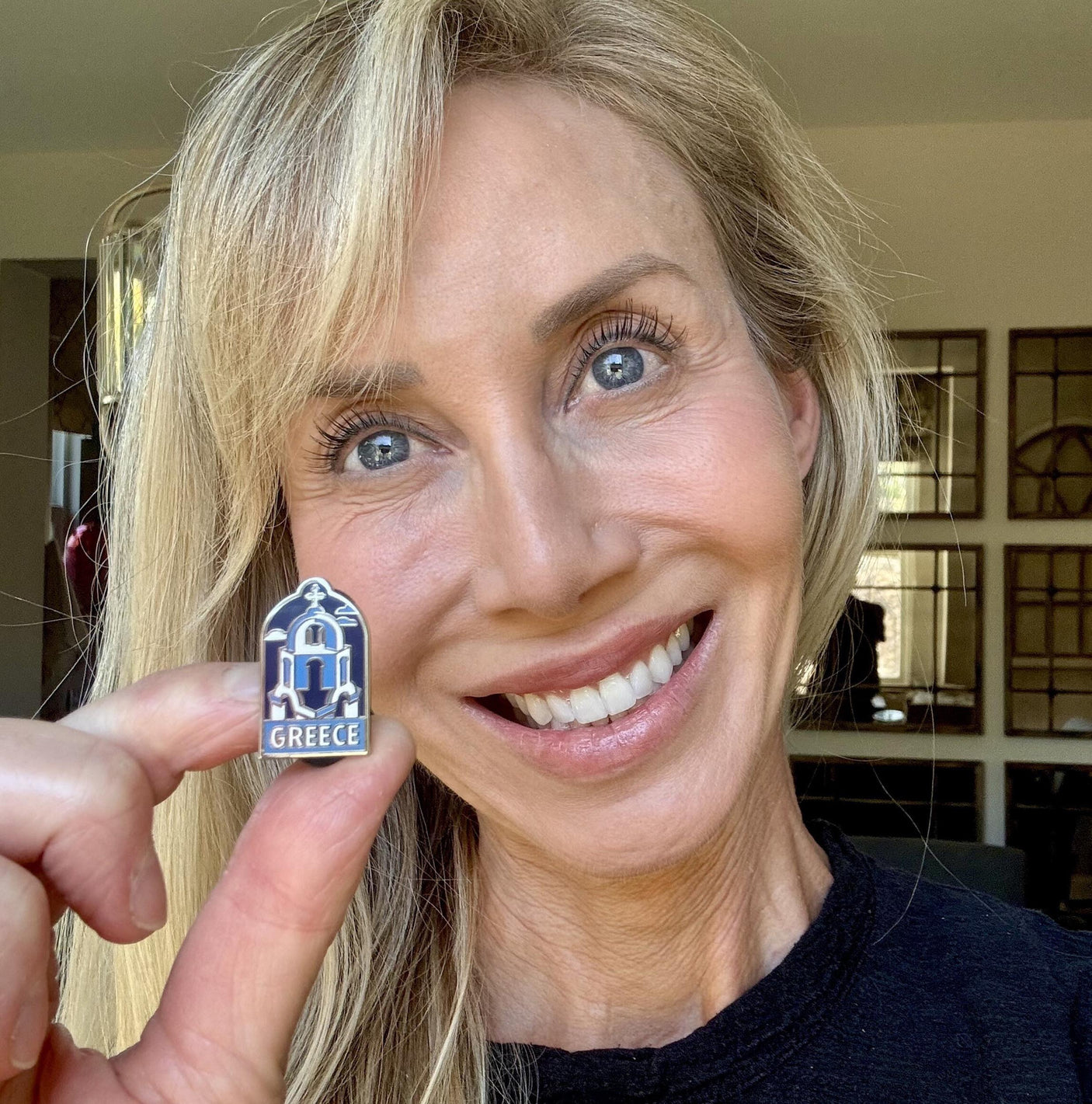 Greece enamel pin featuring a blue and white church design held by a smiling person.