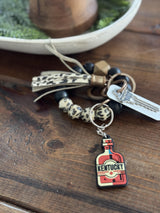Kentucky keychain featuring a bottle design, surrounded by decorative beads and key rings on a wooden surface.